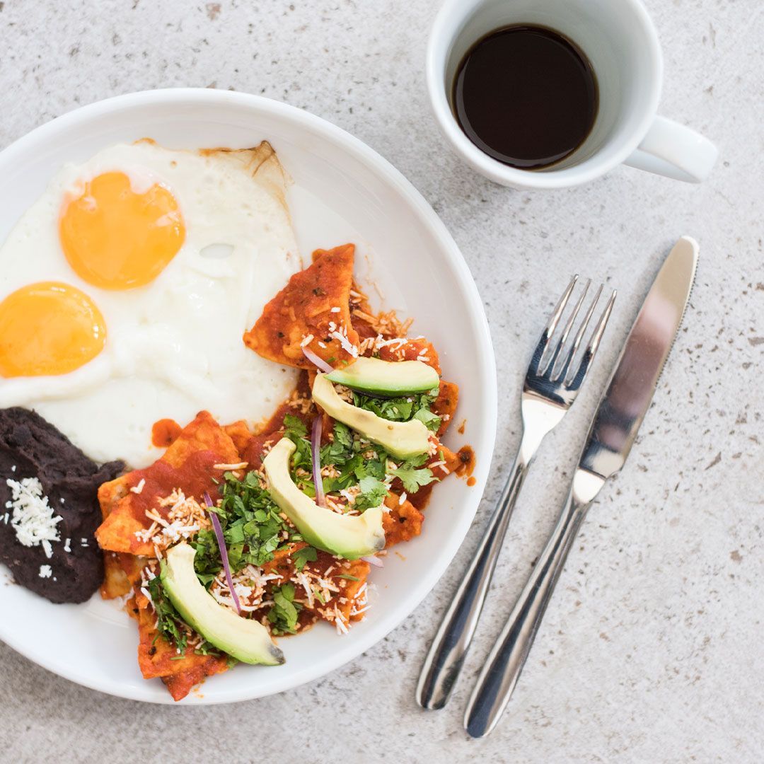 Chilaquiles with eggs, avocado, black beans, and coffee on a white plate.