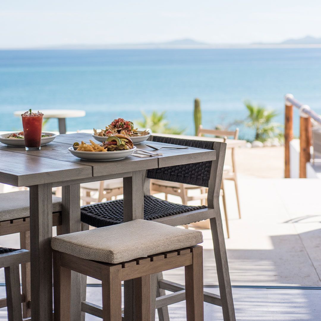 Outdoor dining table with food and drink, overlooking the ocean.