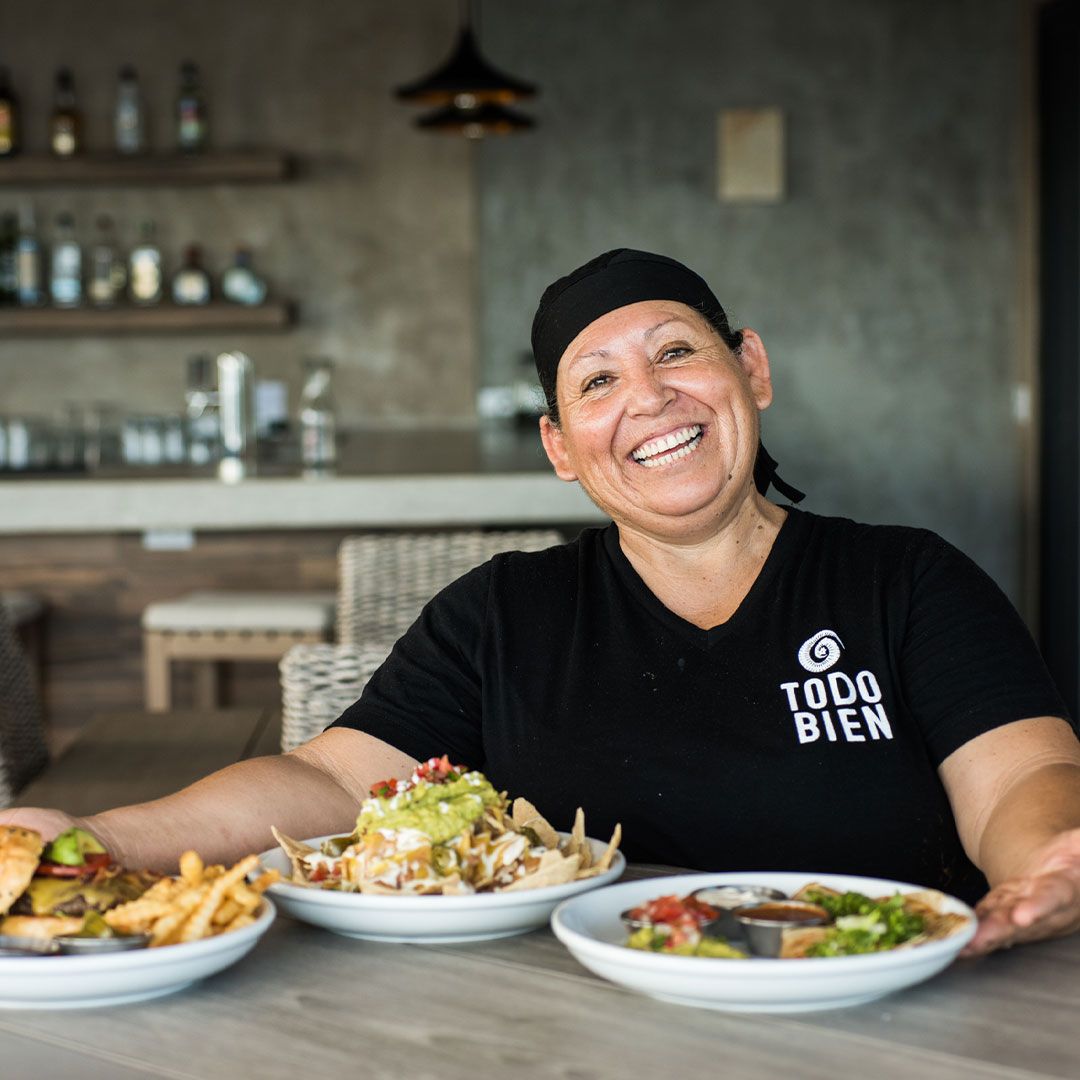Woman smiling at restaurant table with plates of food.