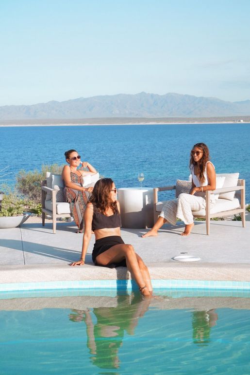 Three people relaxing by a pool overlooking the ocean. Sunny day.