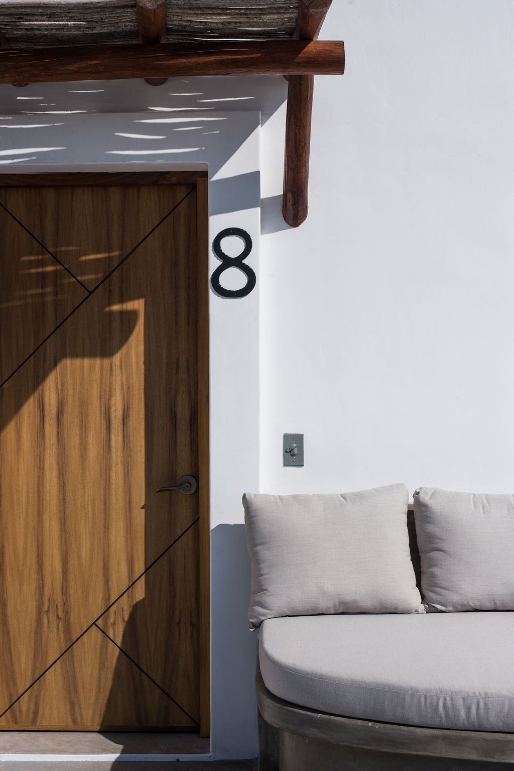 Wooden door with number 8 on white wall, with a seating area and wood pergola.