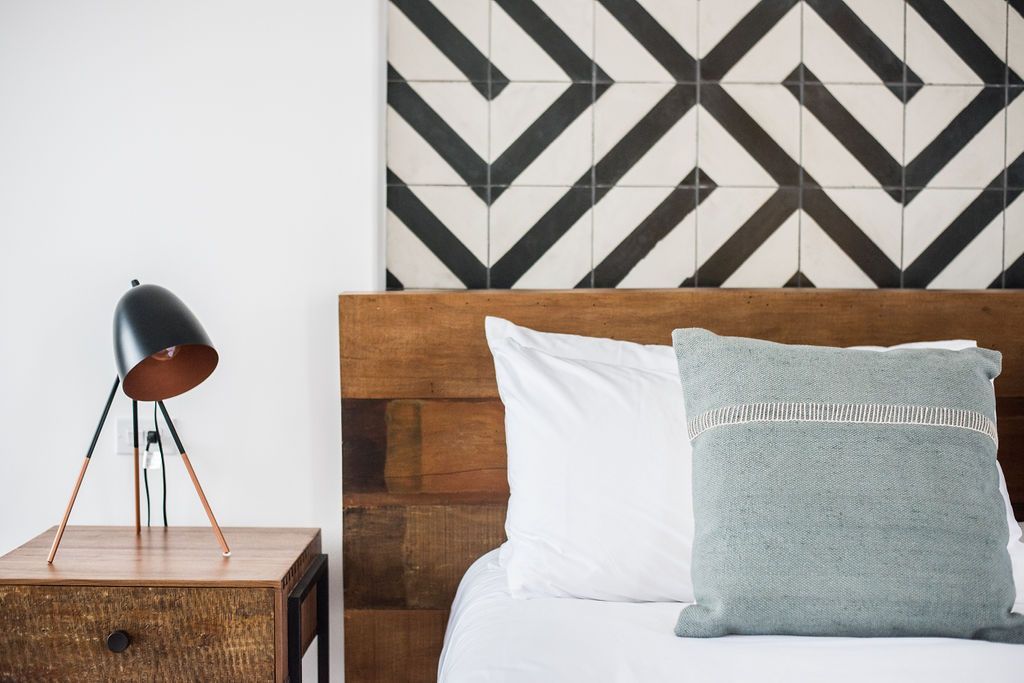 Bedroom with wooden nightstand, bed, and black and white patterned wall tiles.