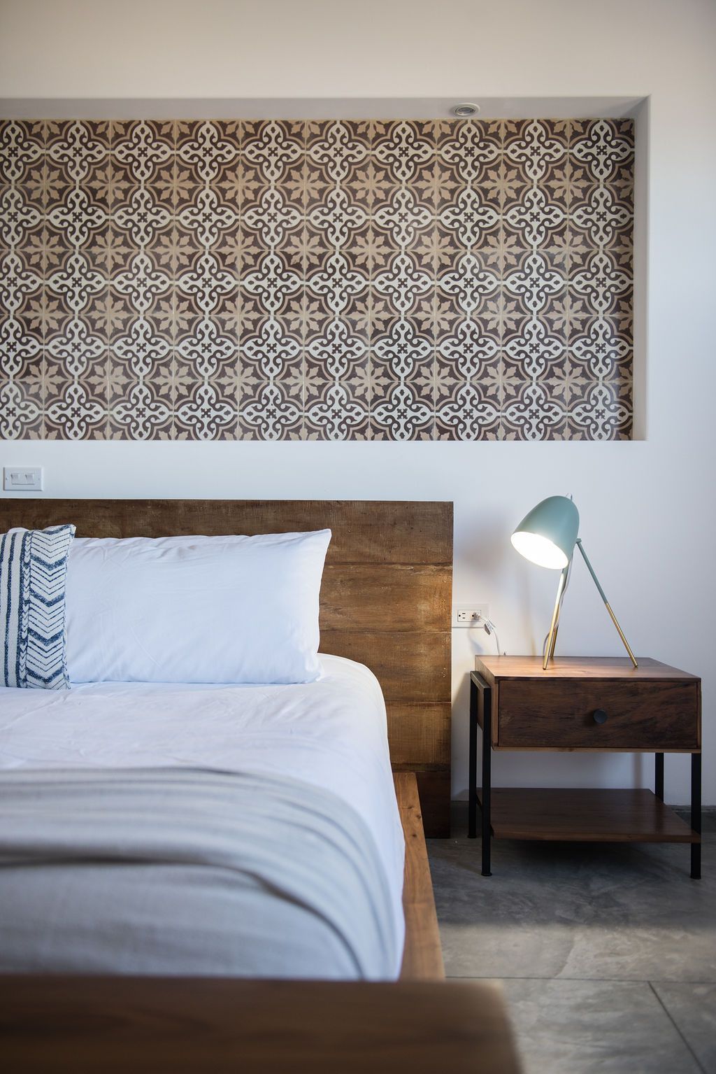 Bedroom with wooden bed, patterned tile wall, and teal bedside lamp on a nightstand.