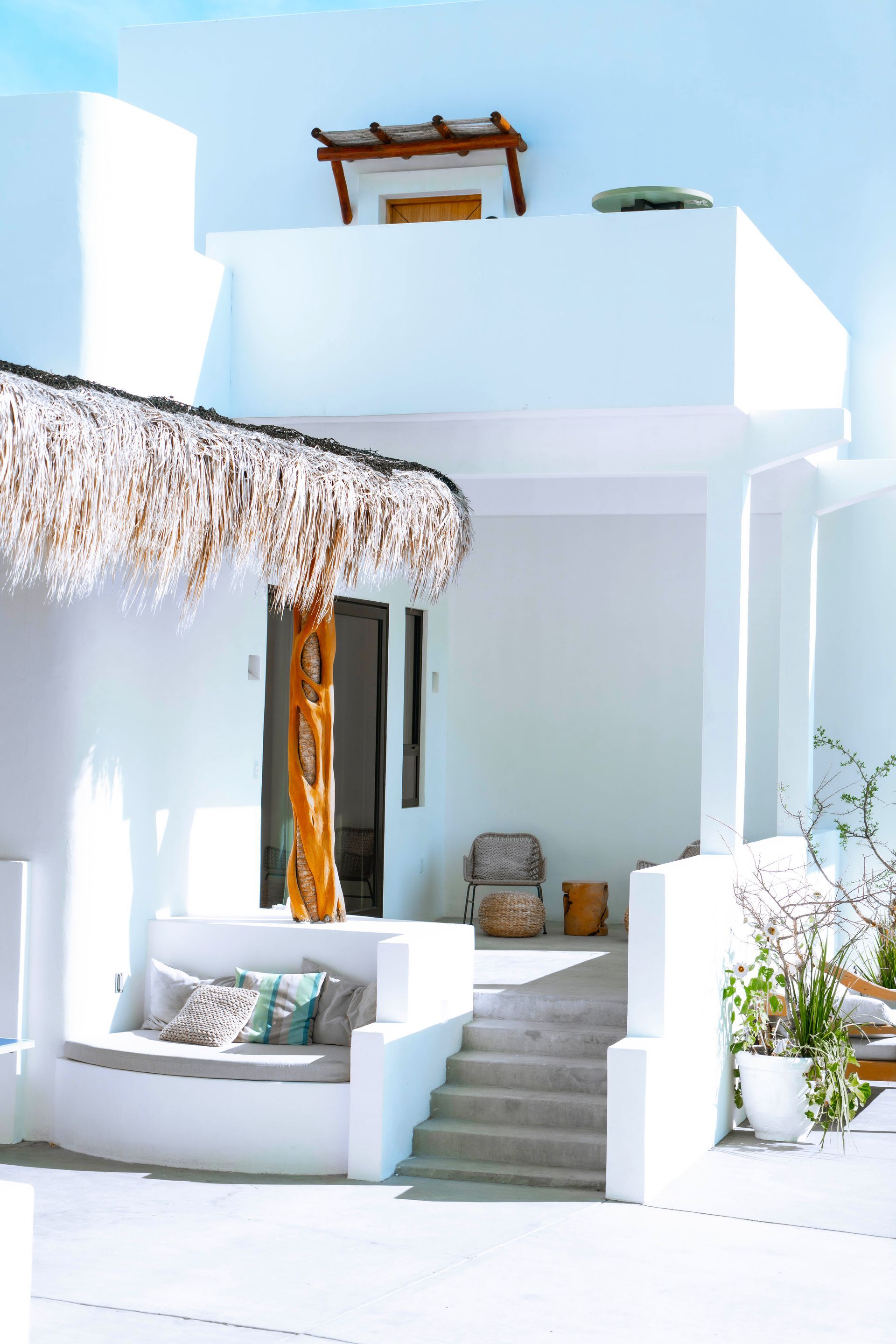 White stucco building with thatch roof and steps leading to a doorway, outdoor seating.