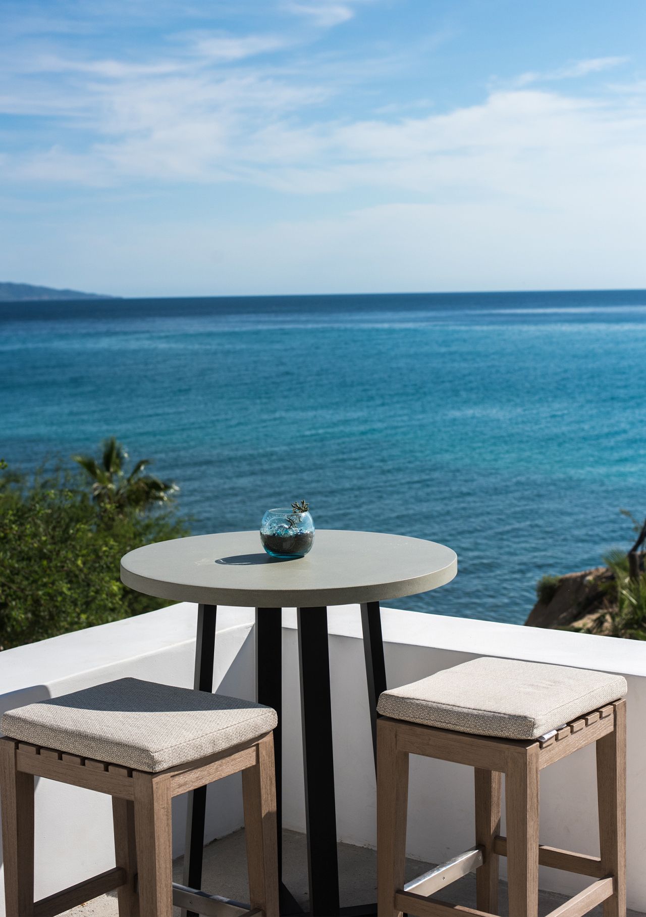 Table with stools on a balcony overlooking the turquoise ocean and blue sky.