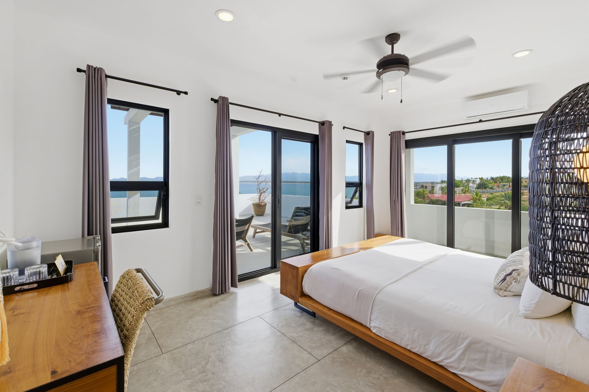 Bedroom with a bed, desk, and large windows overlooking the sea.
