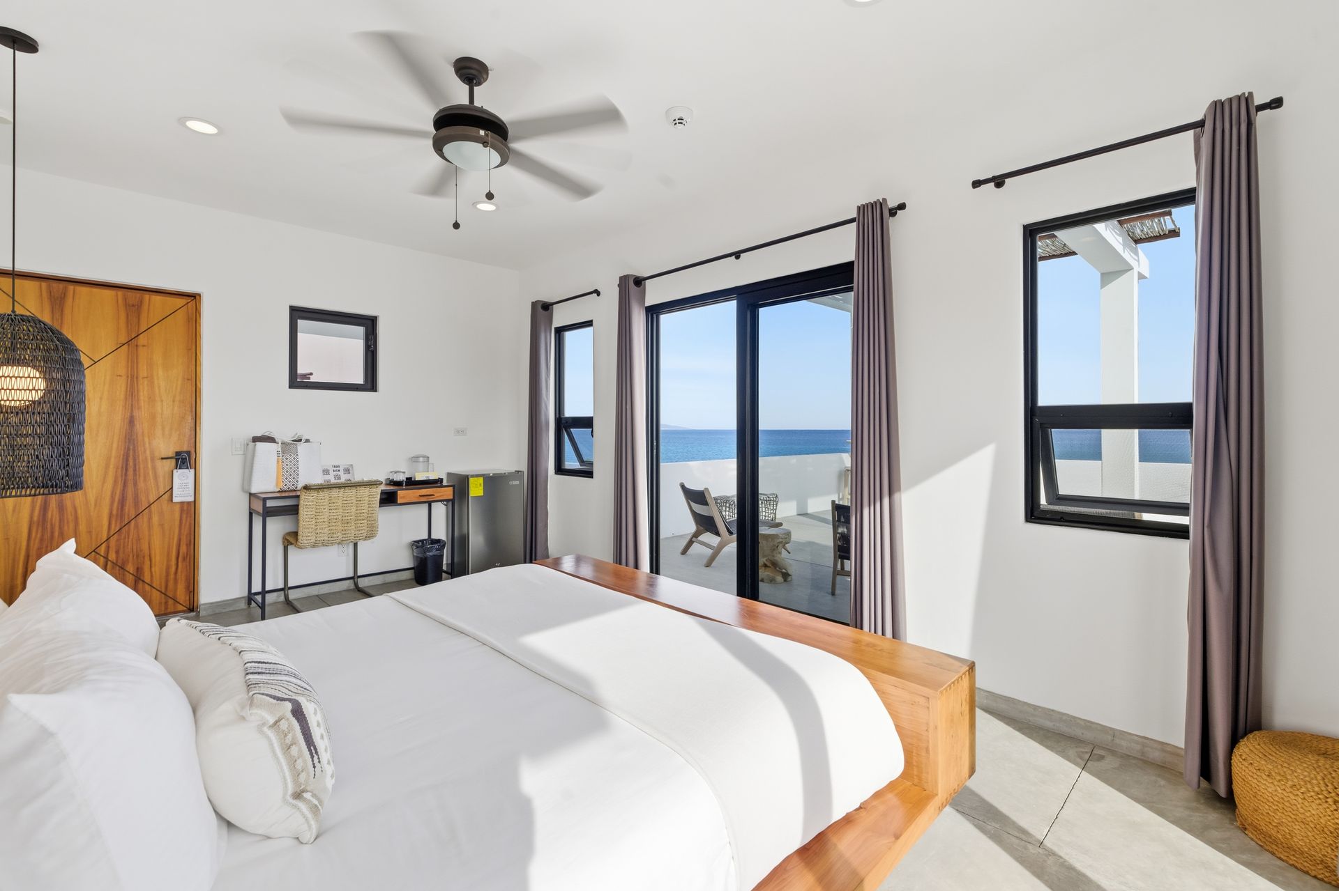 Bedroom with a bed, desk, and ocean view through sliding glass doors.