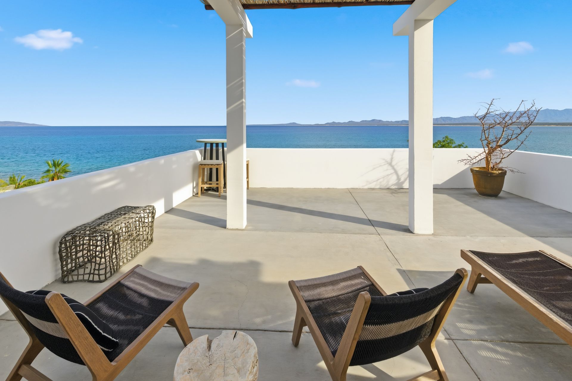 Ocean view patio with lounge chairs under a pergola, blue water, sunny day.