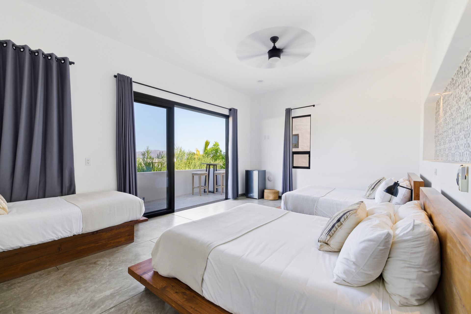 Bedroom with three beds, a balcony, and gray curtains. Bright and airy interior.