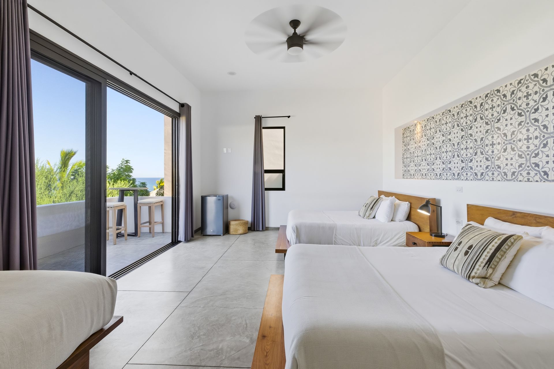 Spacious hotel room with three beds, sliding doors to a balcony, and a decorative wall pattern.