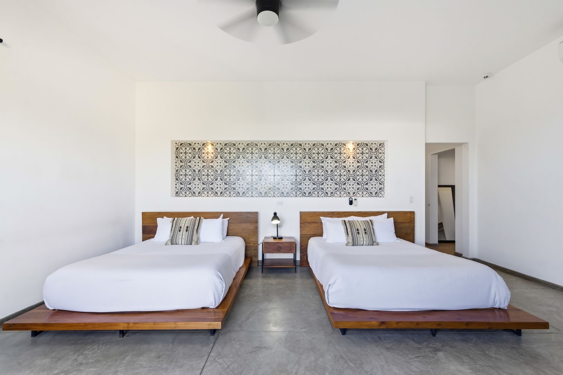 Two beds in a minimalist white room with wood headboards and a decorative wall panel.