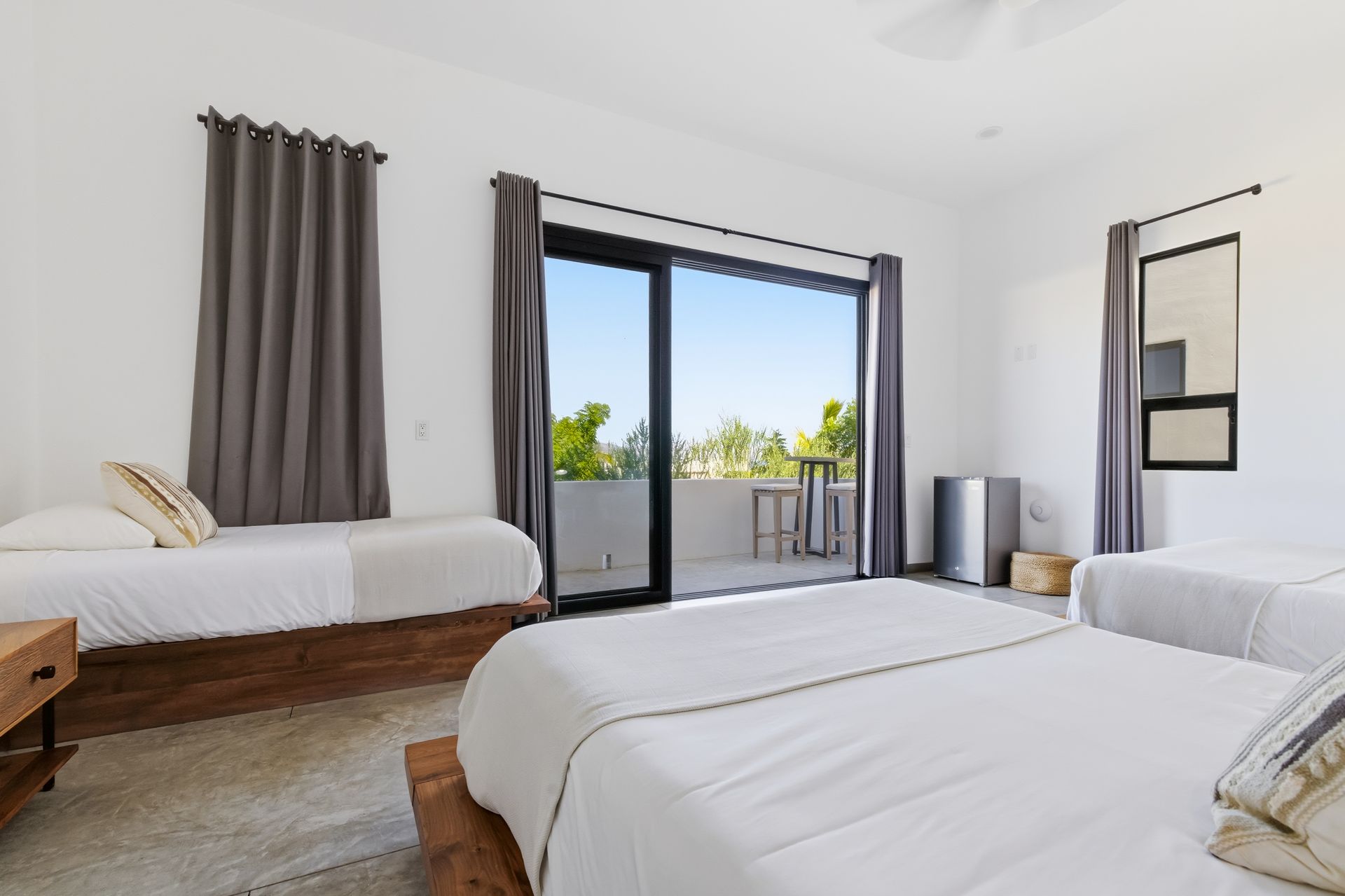 Bedroom with three beds, gray curtains, sliding door to a balcony.
