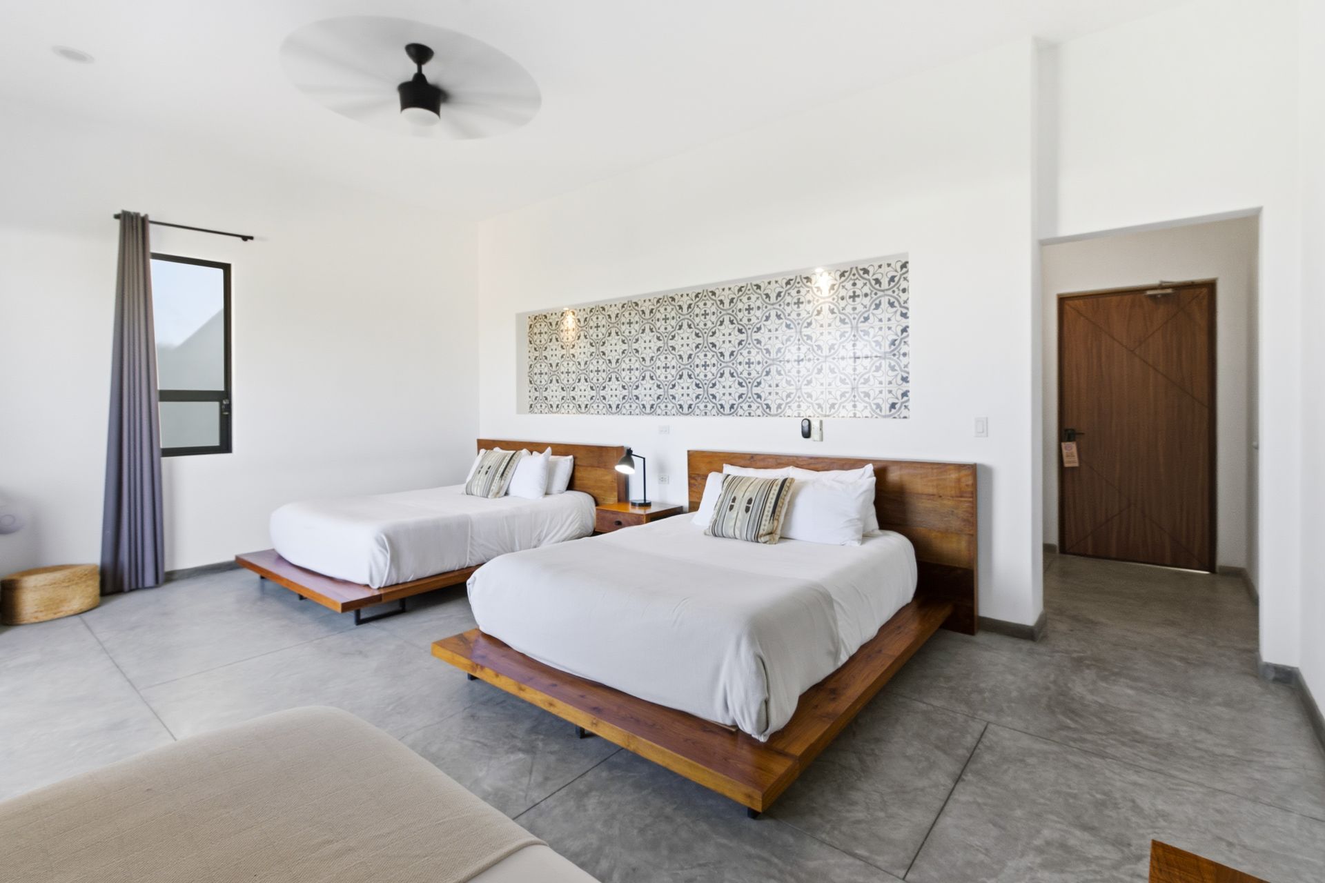 Bright hotel room with two beds, wooden headboards, and a large patterned wall decor.