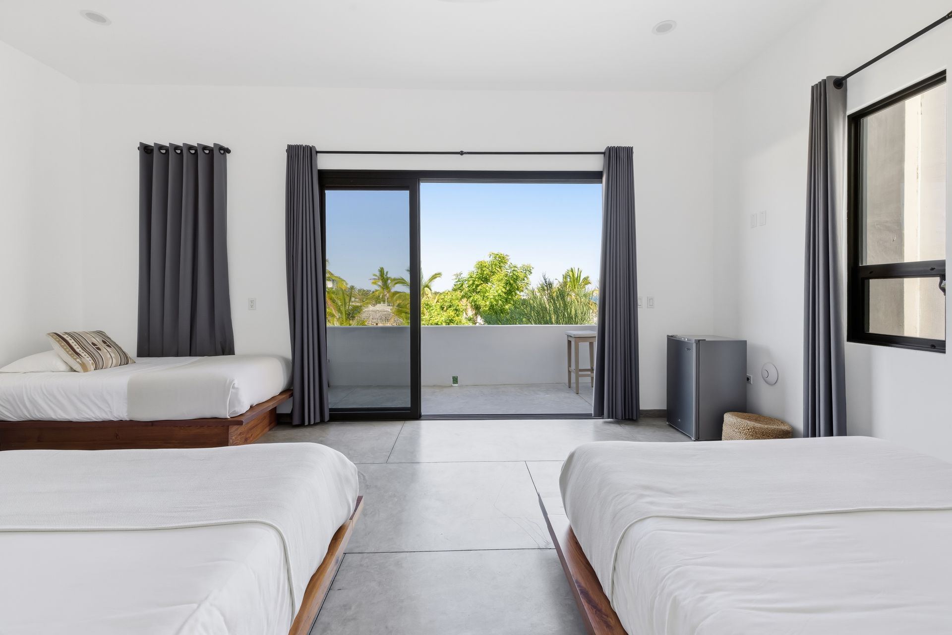 Bedroom with three beds, gray curtains, sliding door to a balcony, white walls.