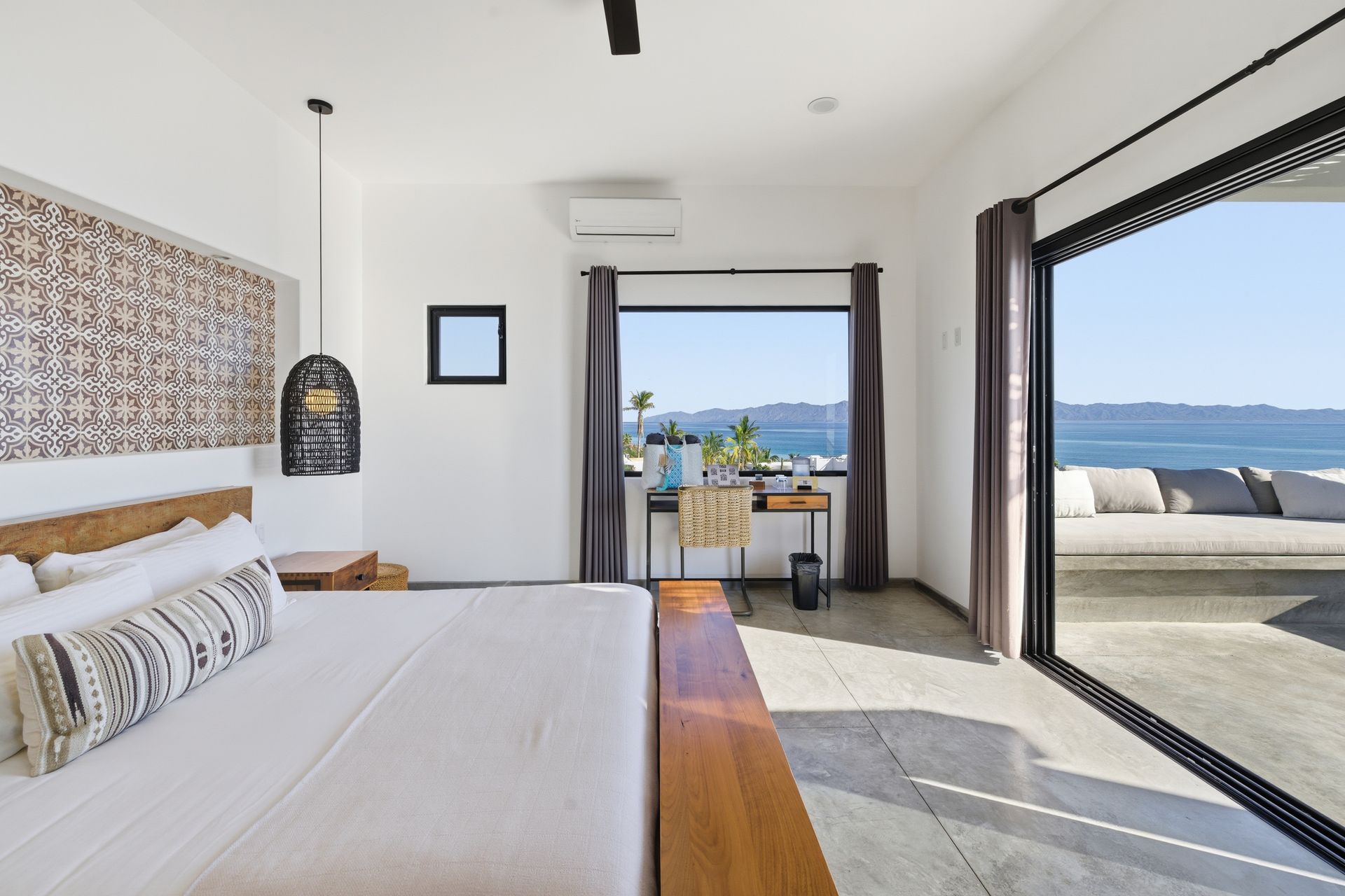 Bedroom with bed, desk, and ocean view through sliding glass door.