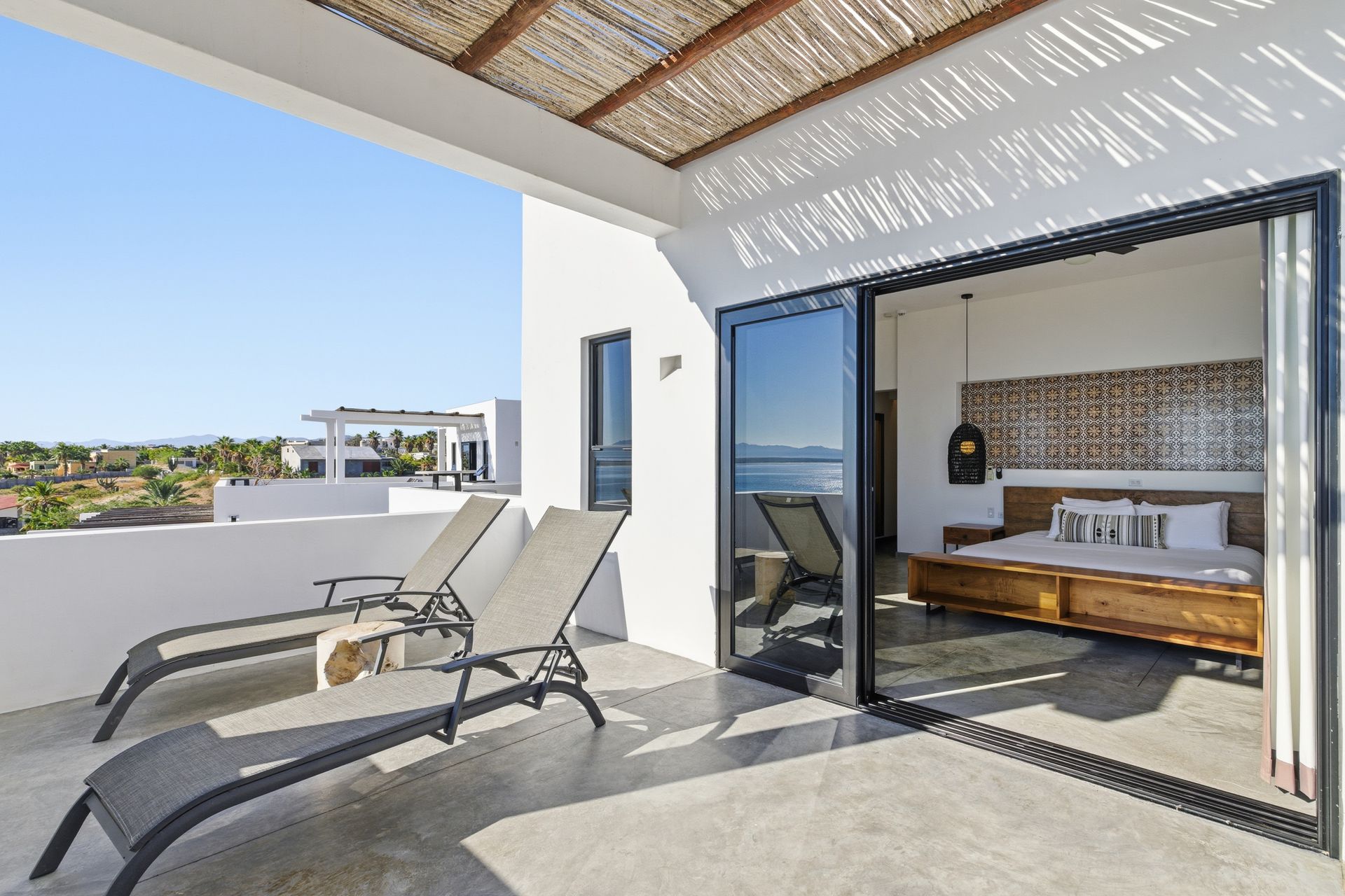 Balcony with two lounge chairs overlooking the ocean, accessed by sliding doors from a bedroom.