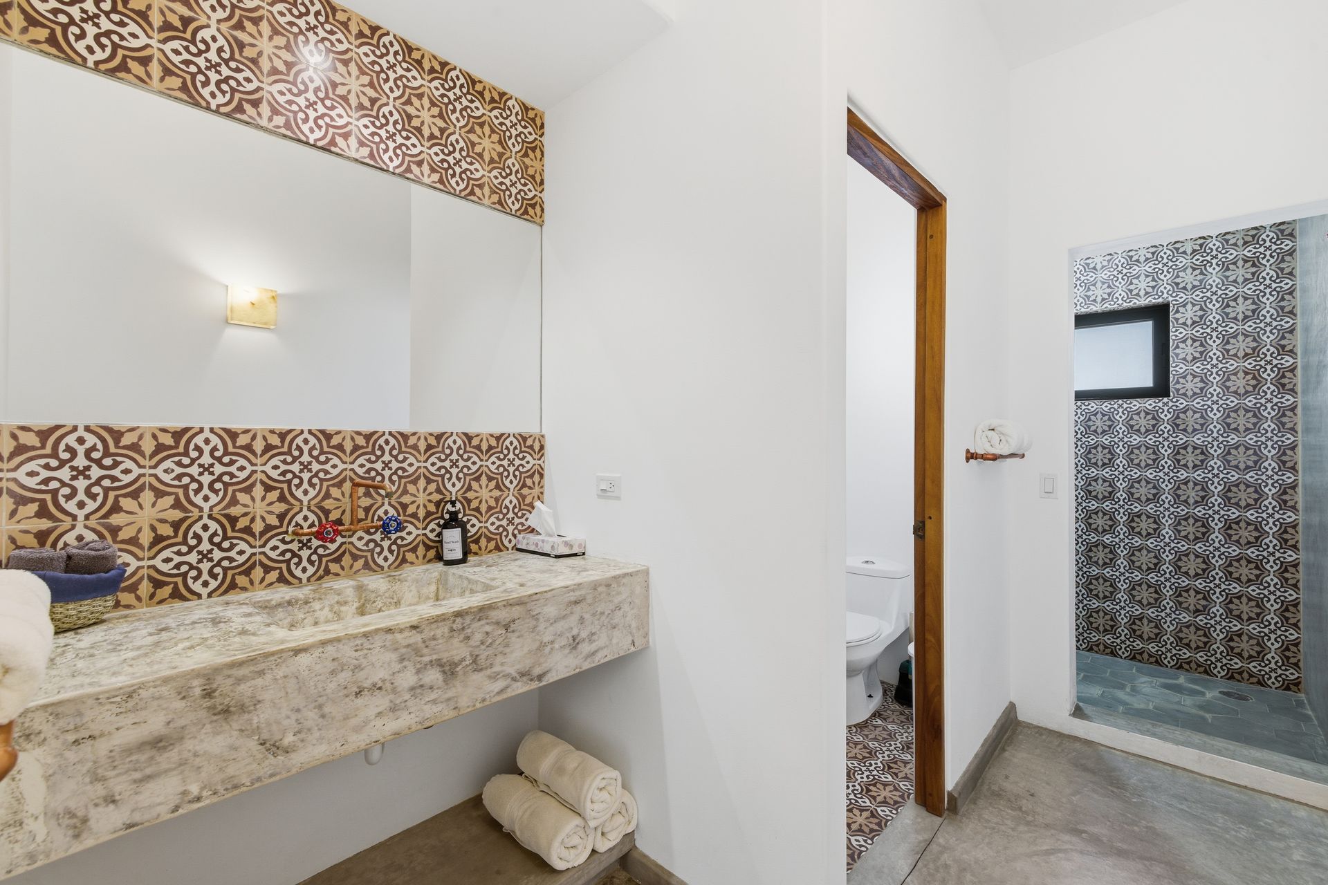 Bathroom with patterned backsplash, stone sink, and open door to a shower and toilet.