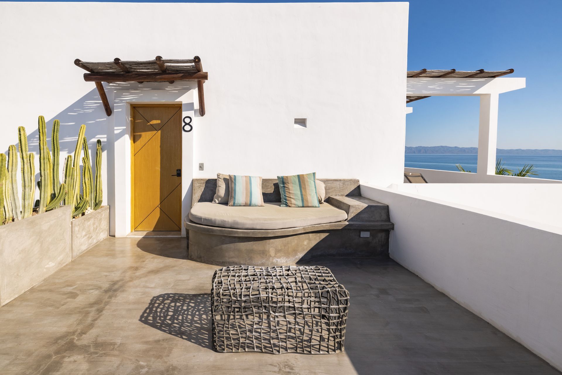 Outdoor patio with white walls, lounge seating, ocean view, and a wooden coffee table.