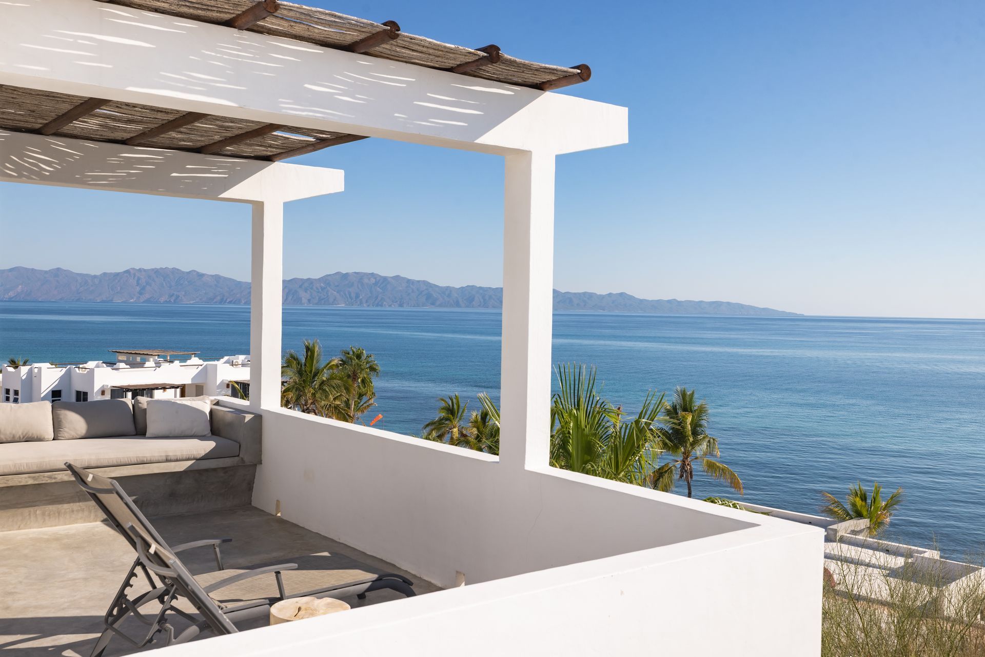 Terrace overlooking a blue sea with mountains in the distance, sunny day.