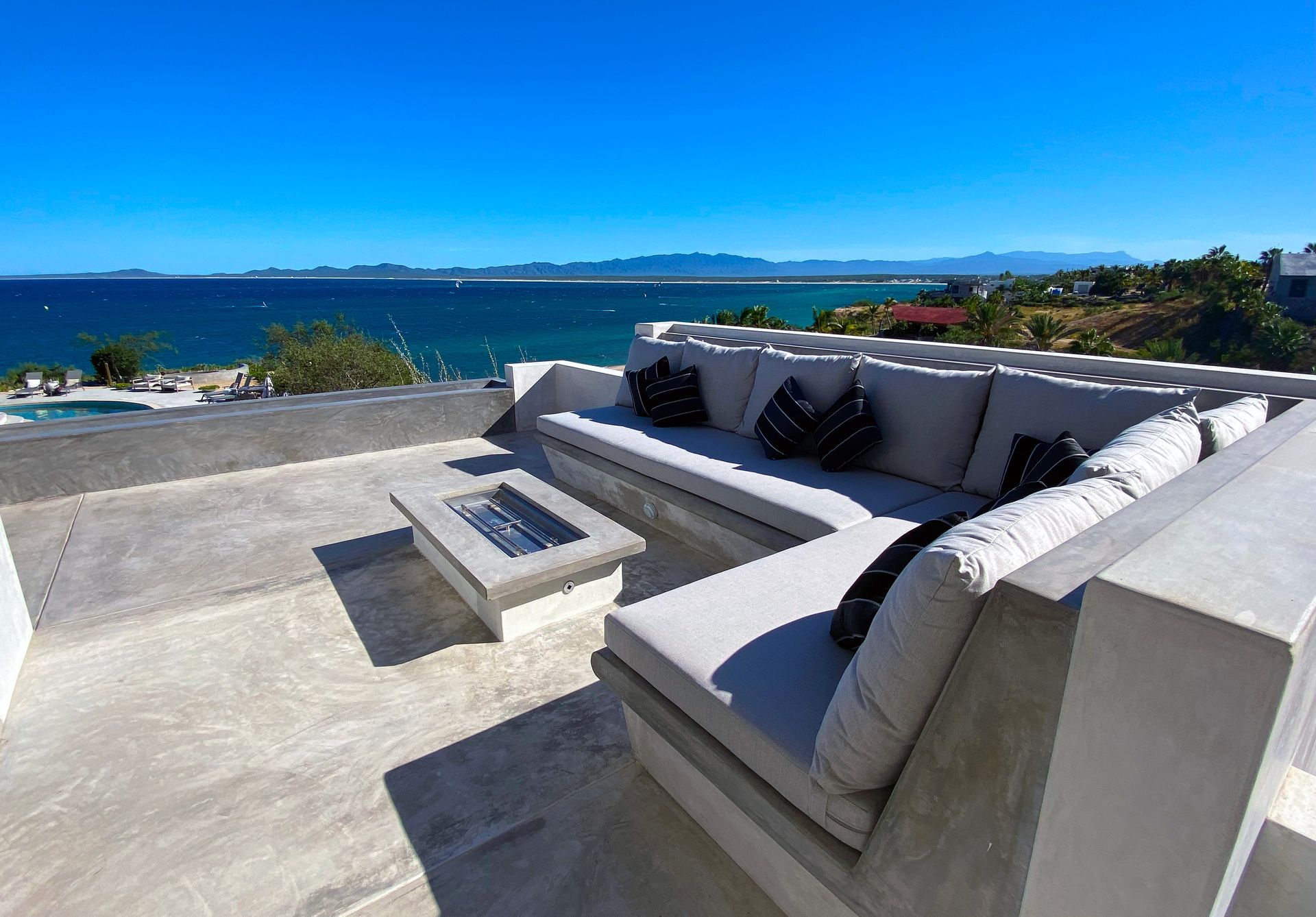 Outdoor seating area overlooking the ocean with a fire pit and blue sky.
