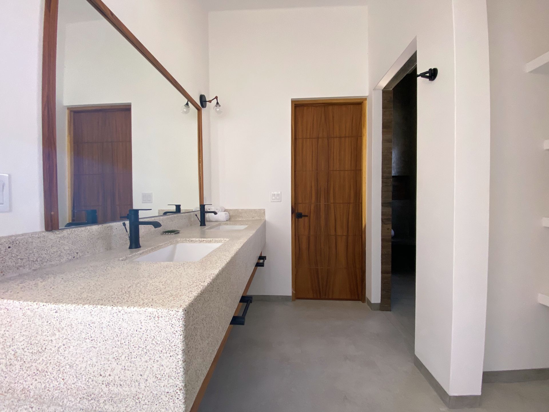Bathroom with a speckled countertop, a large mirror, and a wooden door.