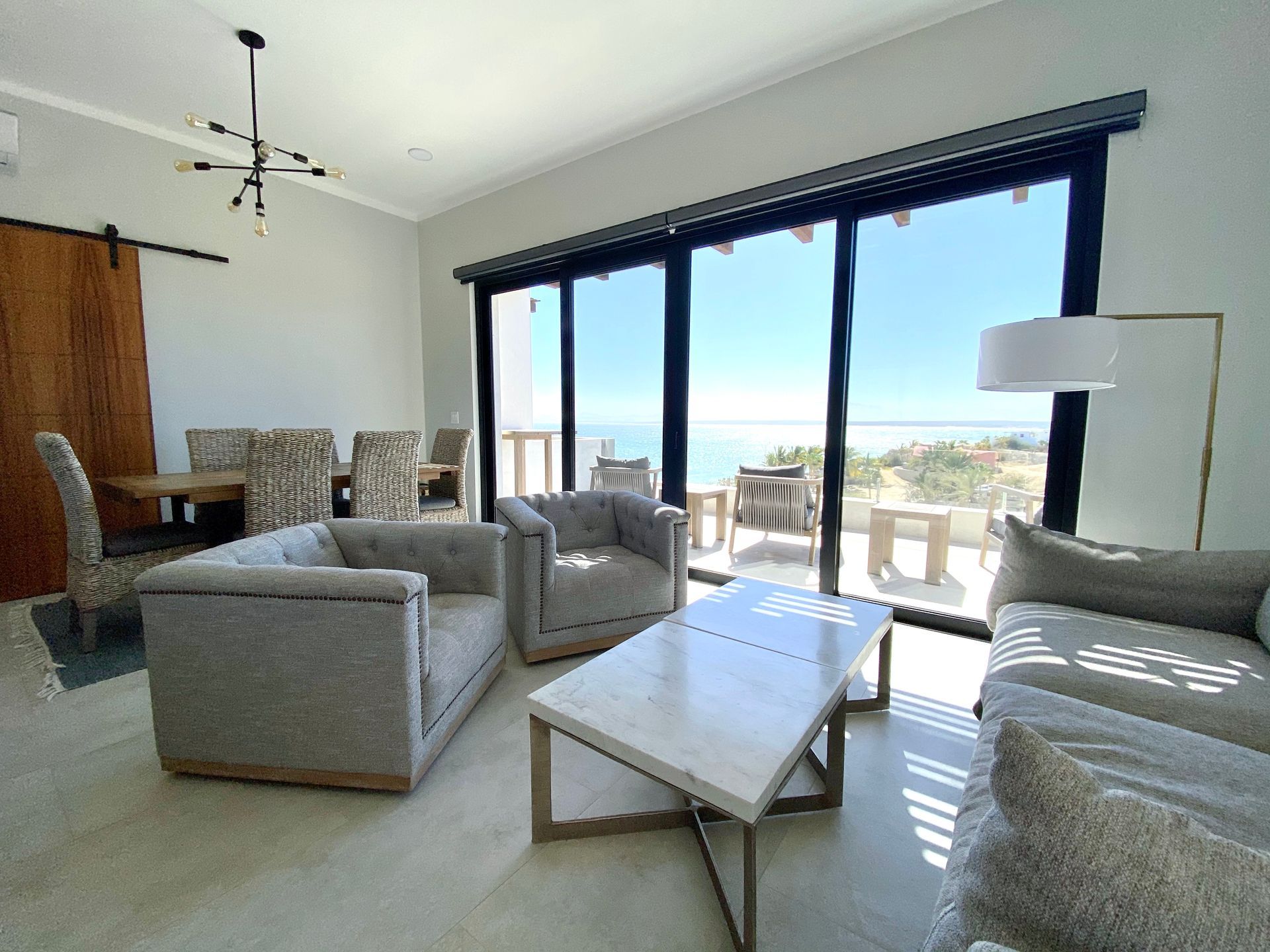 Living room with ocean view, gray sofas, marble coffee table, sliding glass doors, dining area.