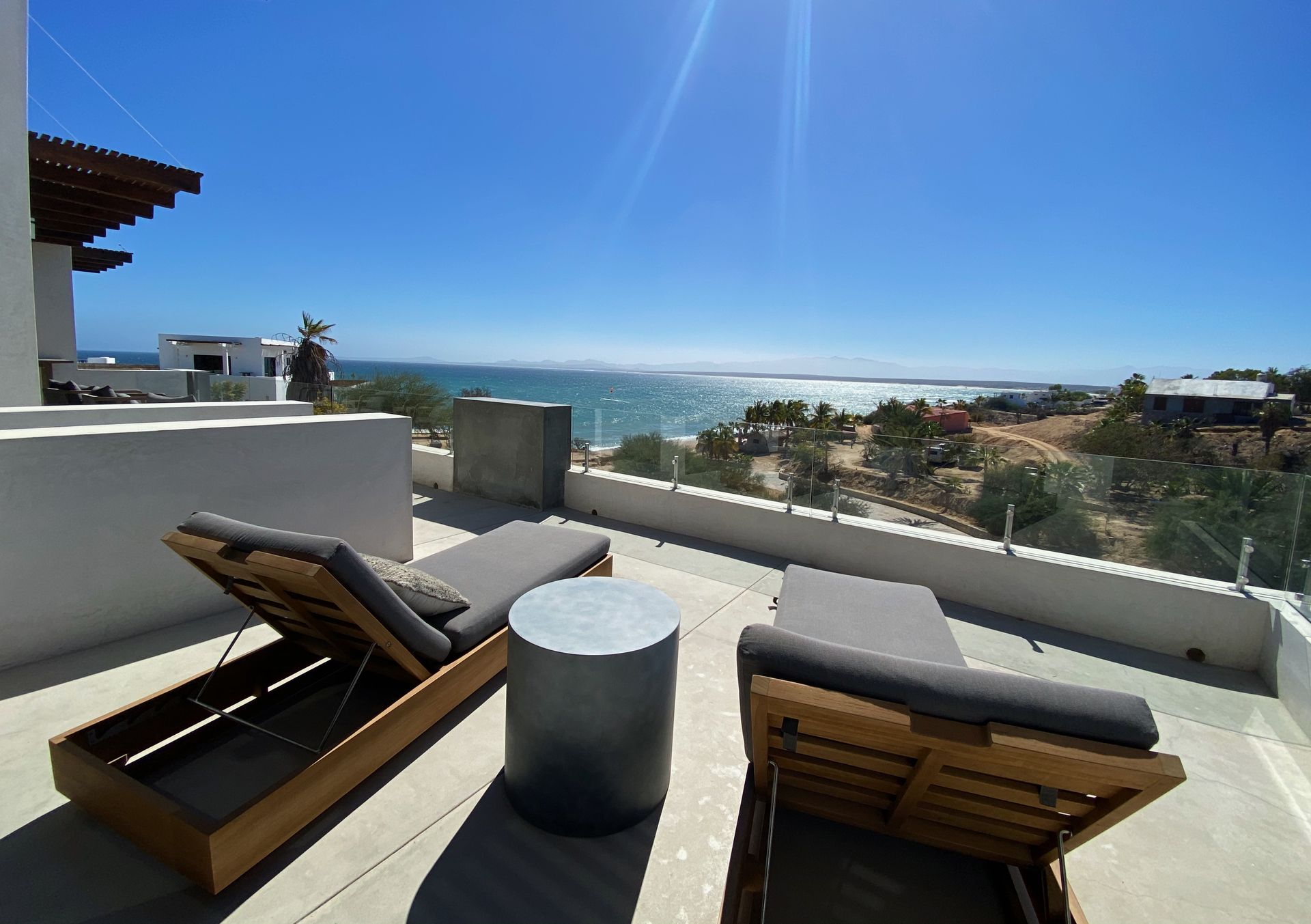 Two lounge chairs face the ocean on a sunny terrace.