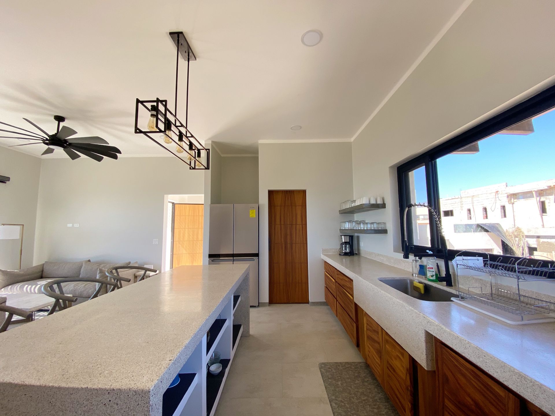 Modern kitchen with a long countertop, wooden cabinets, and large window.