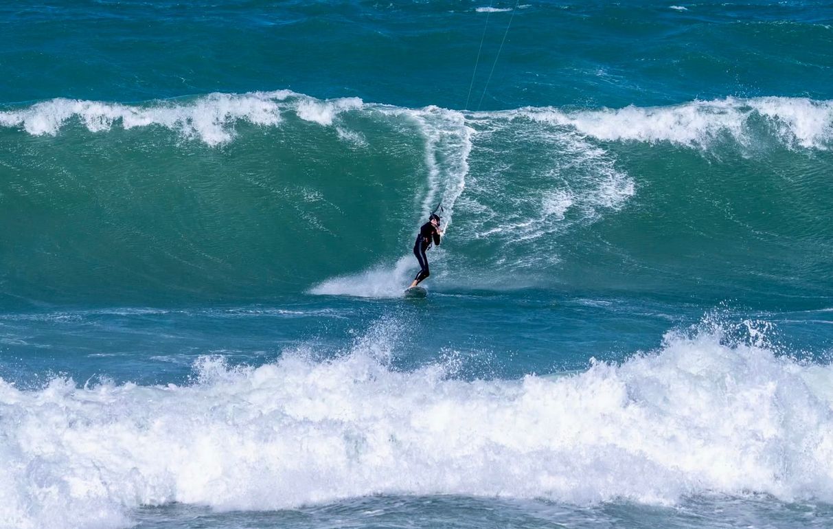 Surfer riding a large turquoise wave, spray erupting. Ocean scene.