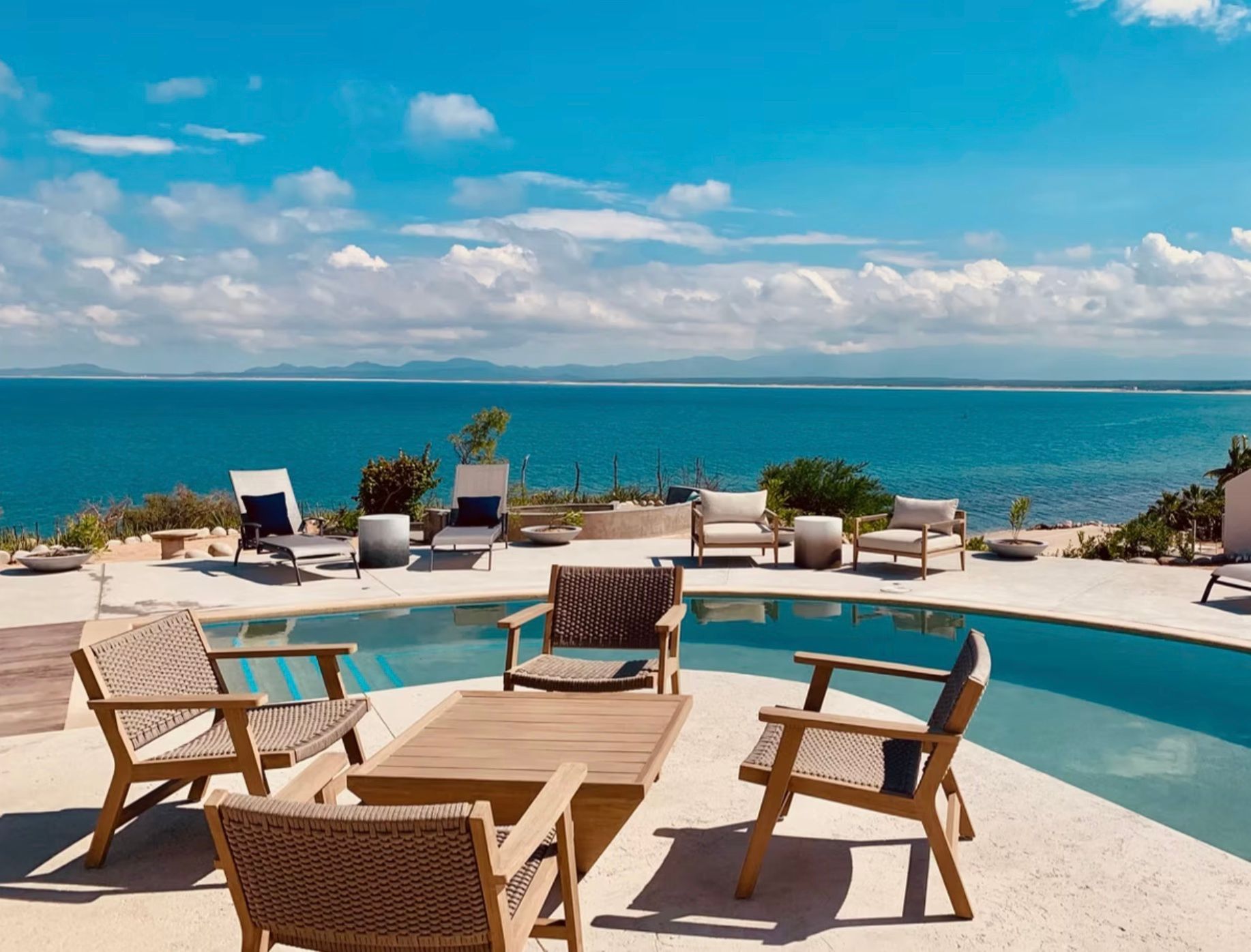 Outdoor seating area with pool overlooking blue ocean under a bright sky.