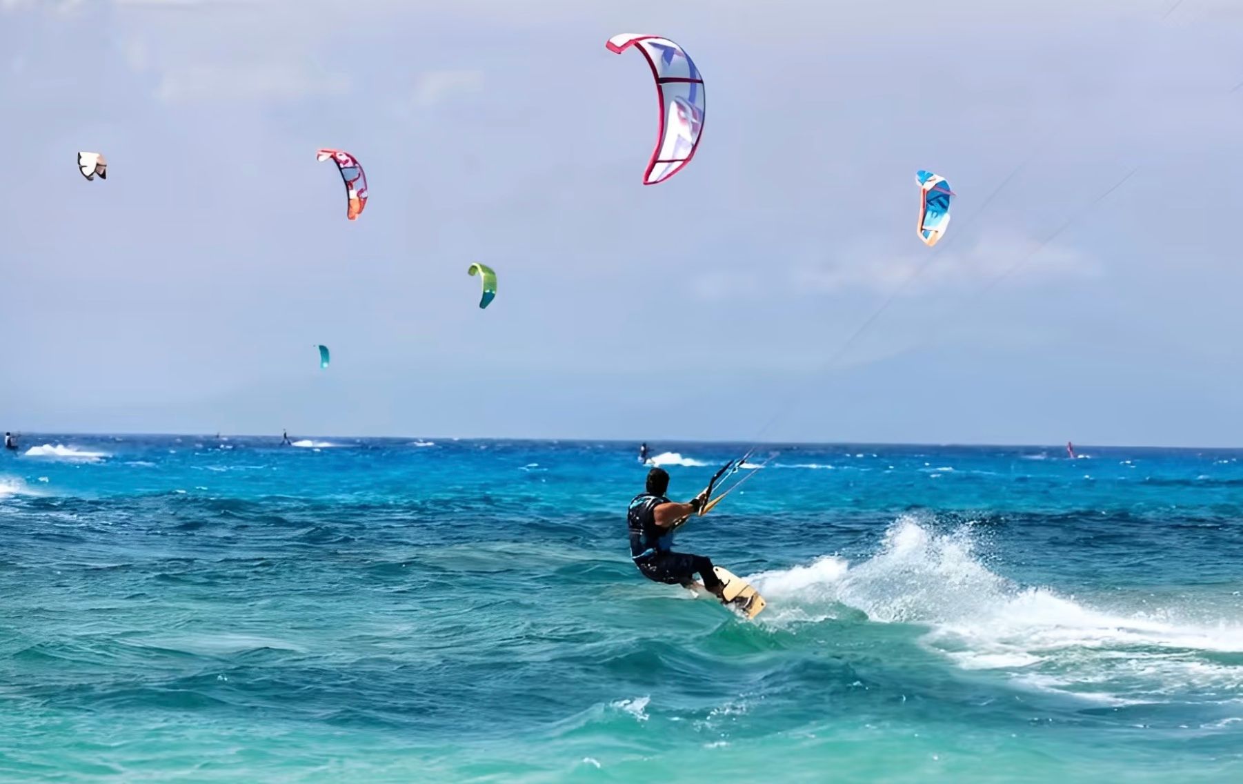 Kitesurfer on blue ocean, multiple kites in the sky. Sunny day.