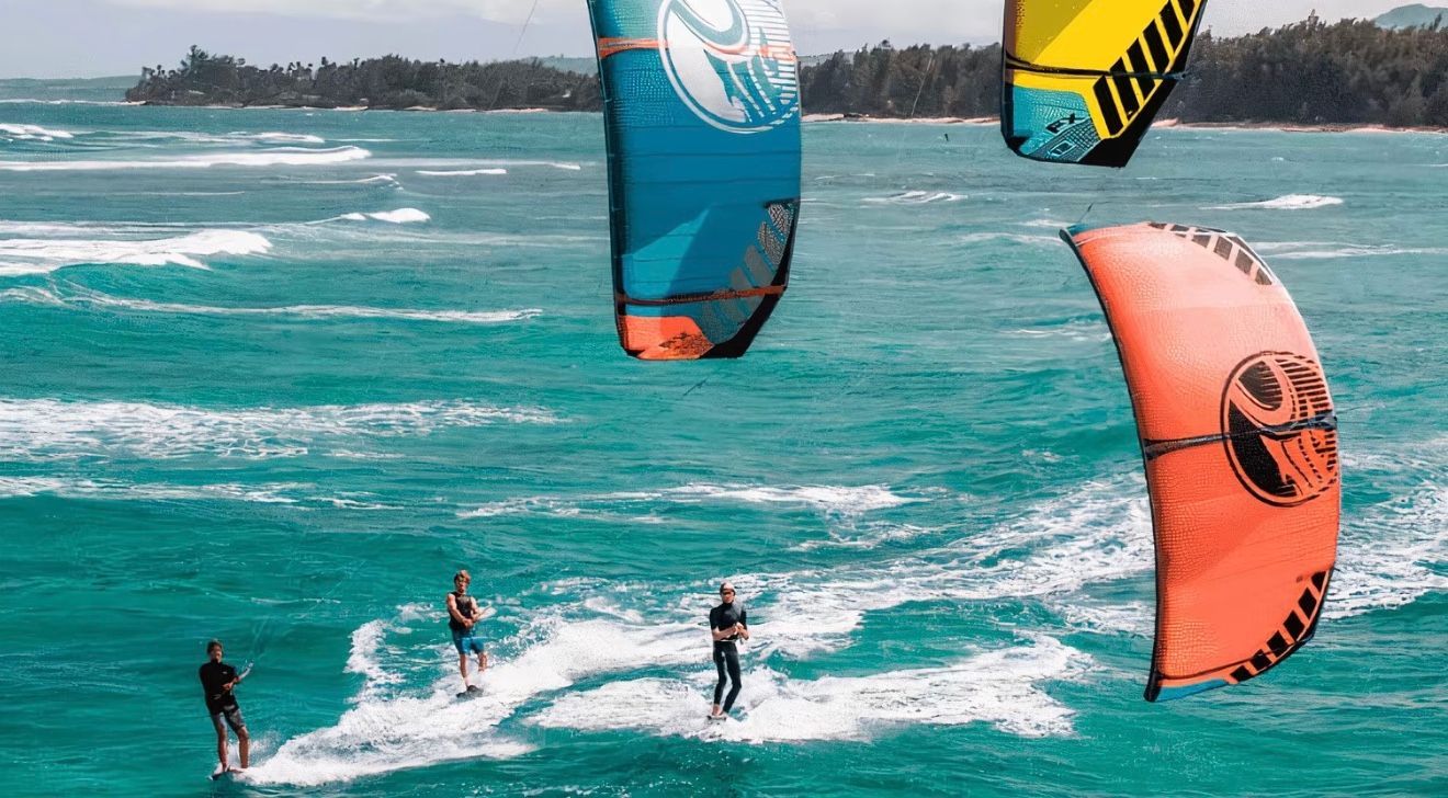 Kiteboarders on turquoise water with colorful kites in the air.