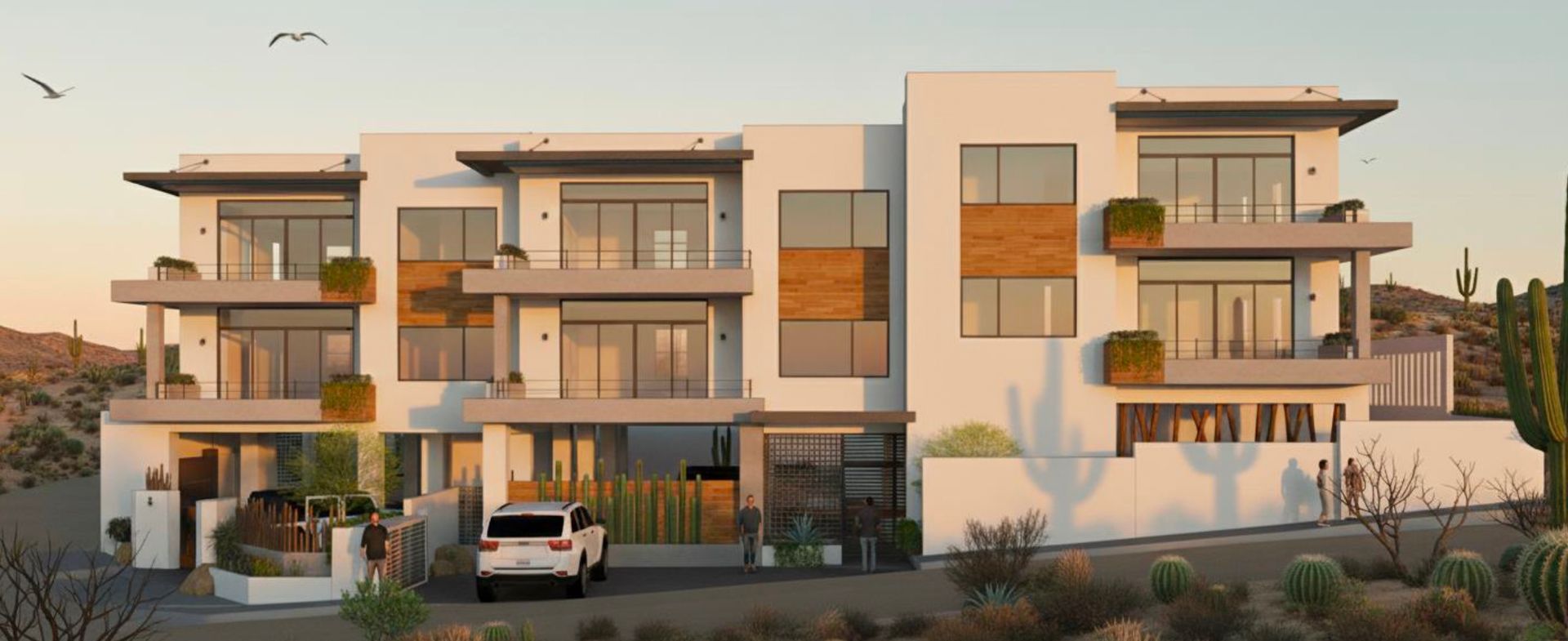 Modern white building with balconies in a desert landscape. A white SUV is parked in front.