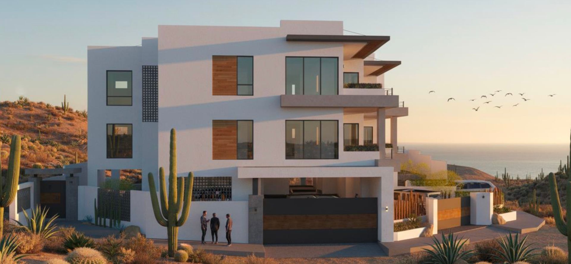 Modern white multi-story house with a view of the ocean. Desert vegetation and a group of people are in front of the house.
