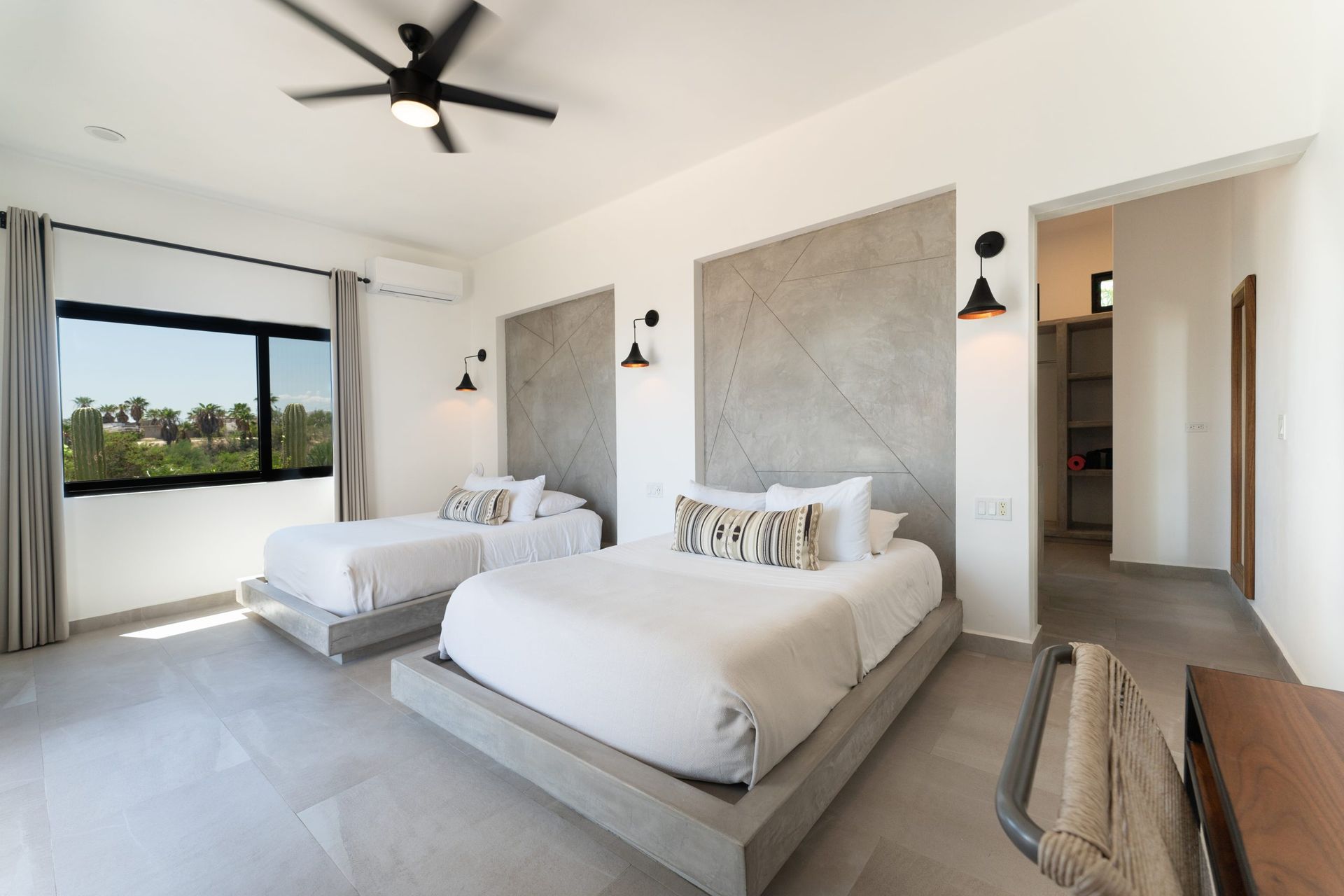 A bright bedroom with two beds, a window, and a ceiling fan.