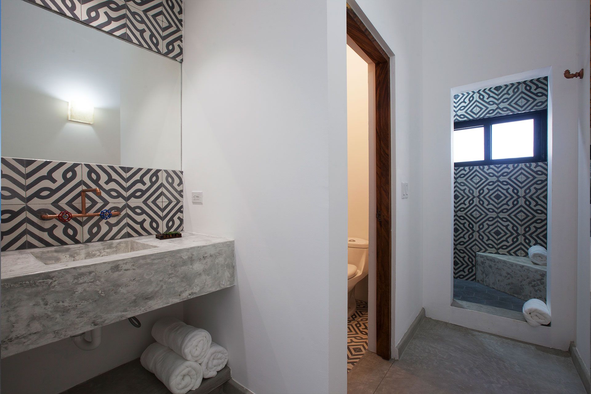 Bathroom with a concrete sink and patterned tile backsplash and accent wall. White walls and towels.