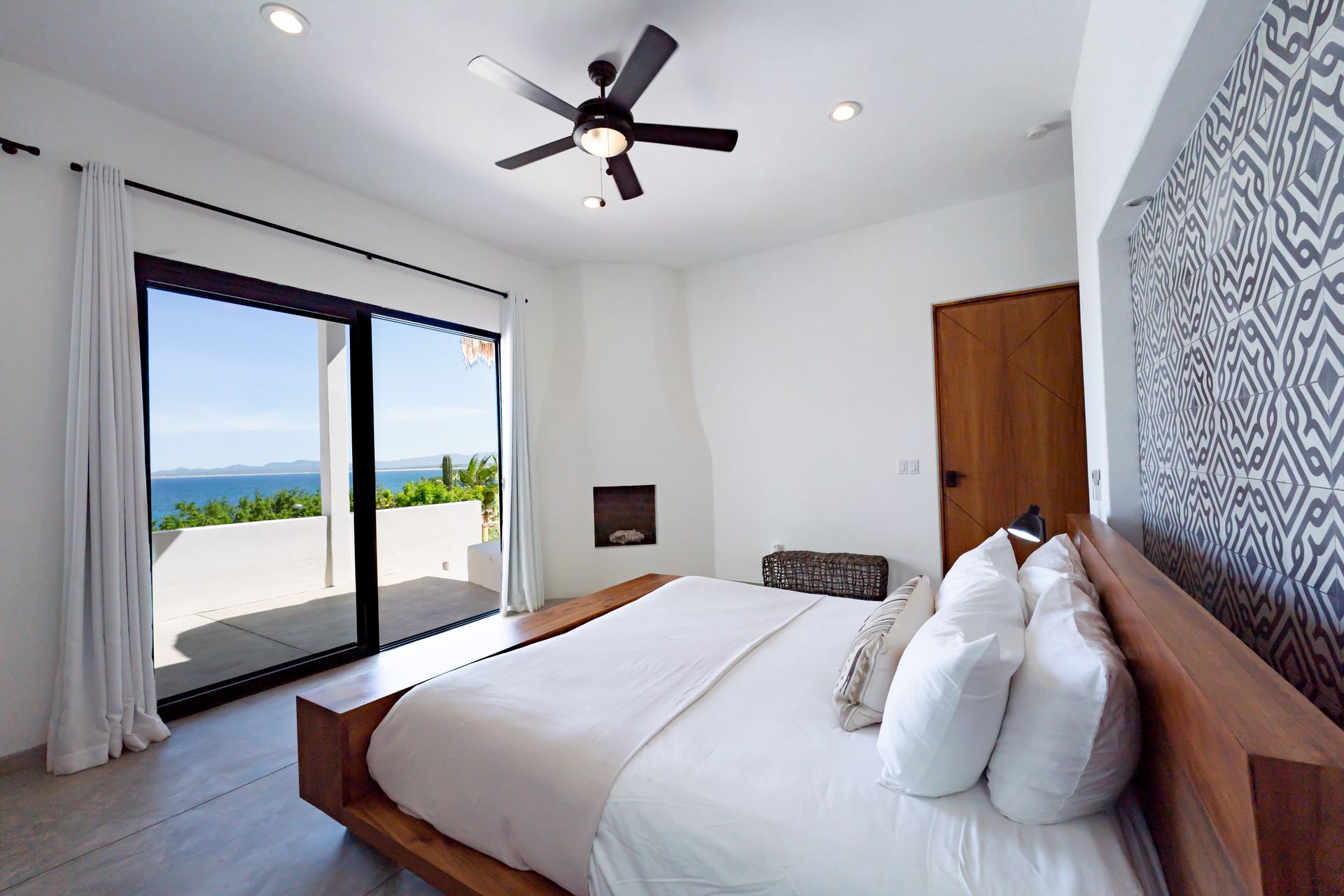 Bedroom with a bed, open glass doors, and a view of the ocean.