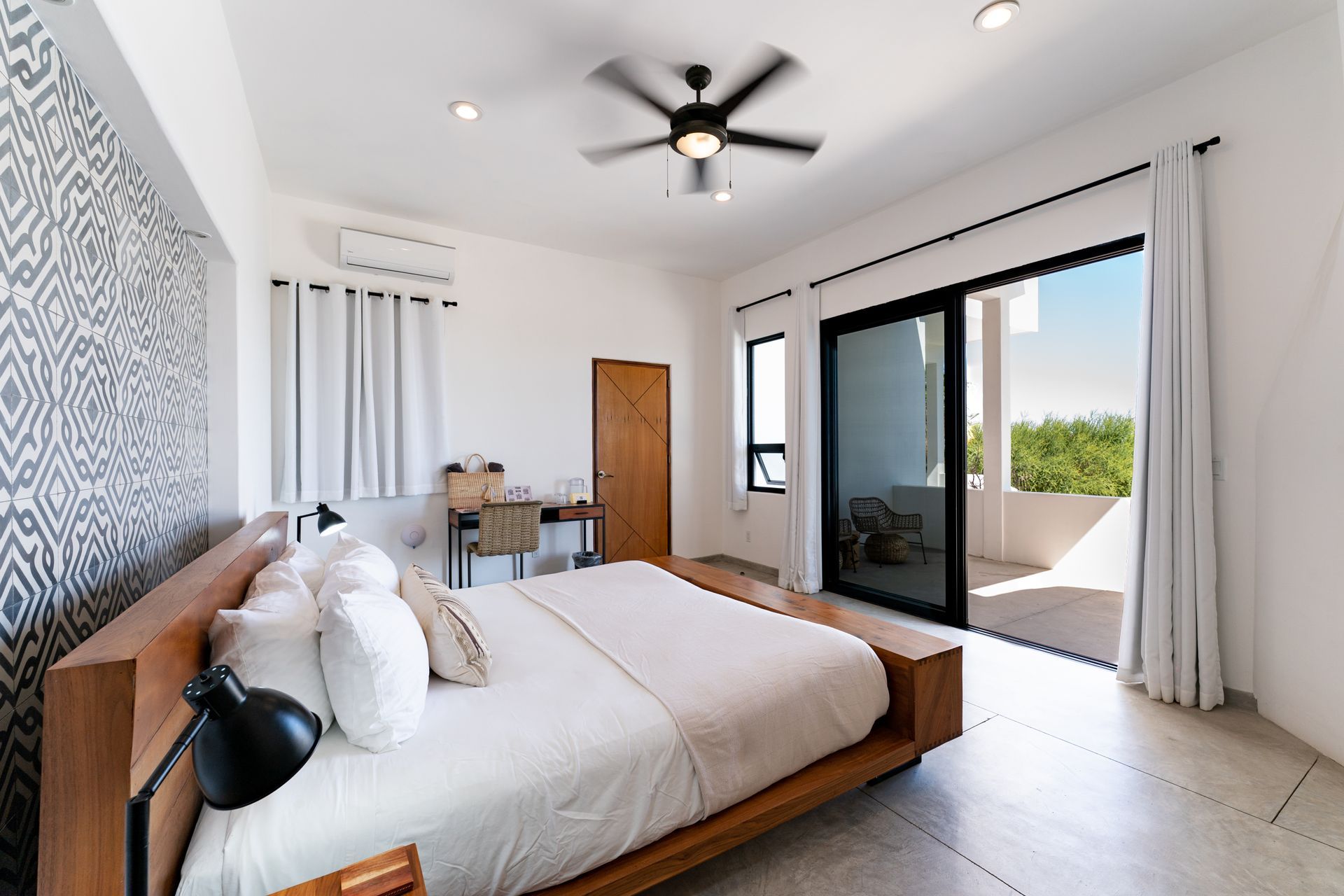 Bedroom with wooden bed, patterned wall, sliding door to balcony, and ceiling fan.