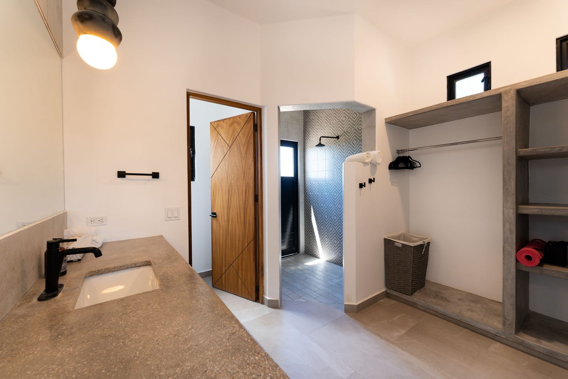 Bathroom with a concrete countertop, open doorway, closet, and shower with gray tile.
