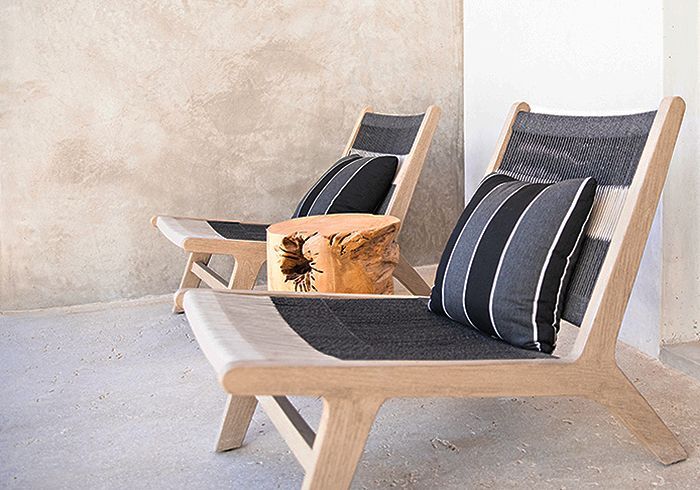 Two wooden lounge chairs with striped pillows and a wooden side table.