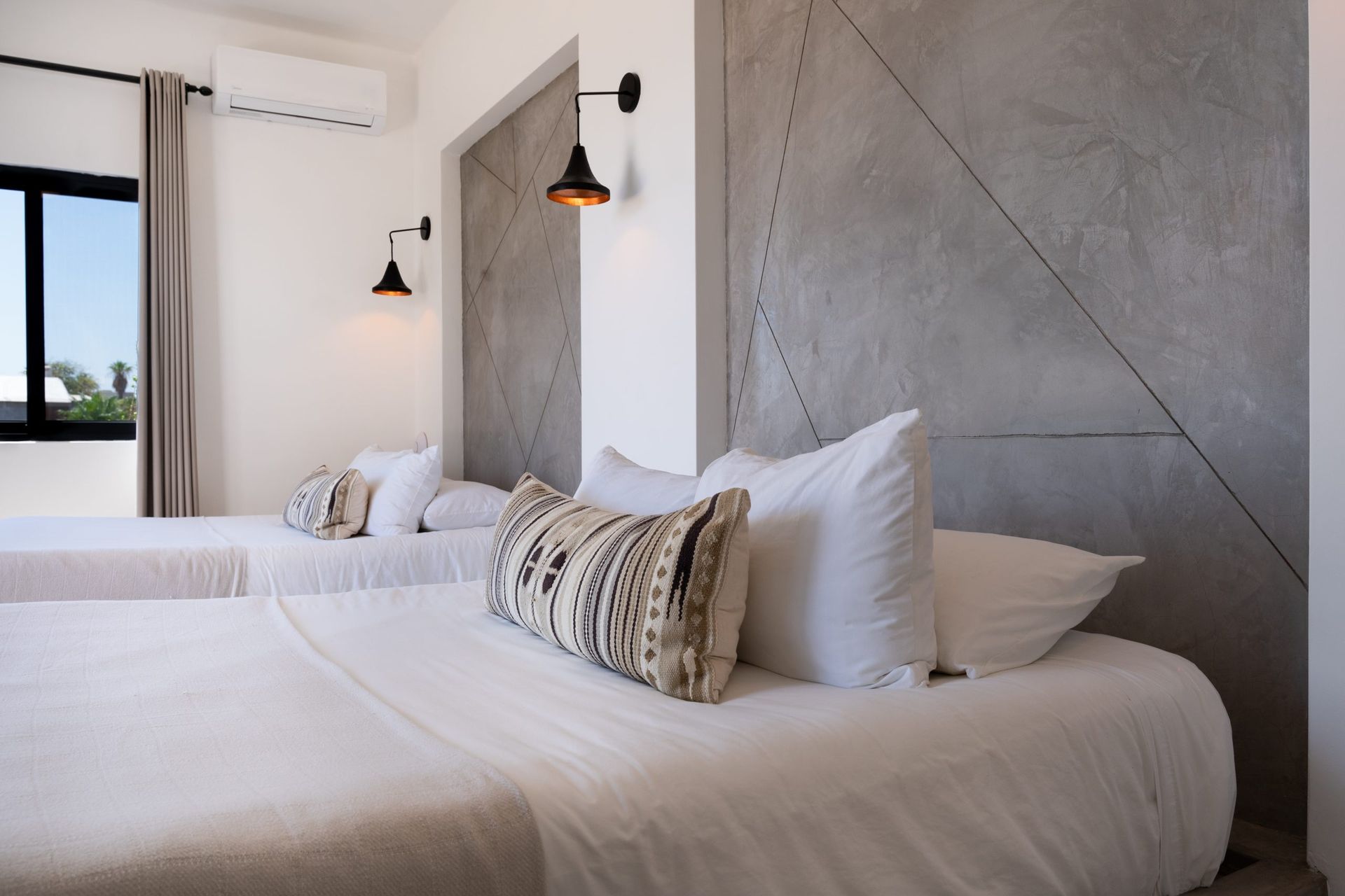 Bedroom with two beds, white bedding, gray accent wall, black sconces, and air conditioner.