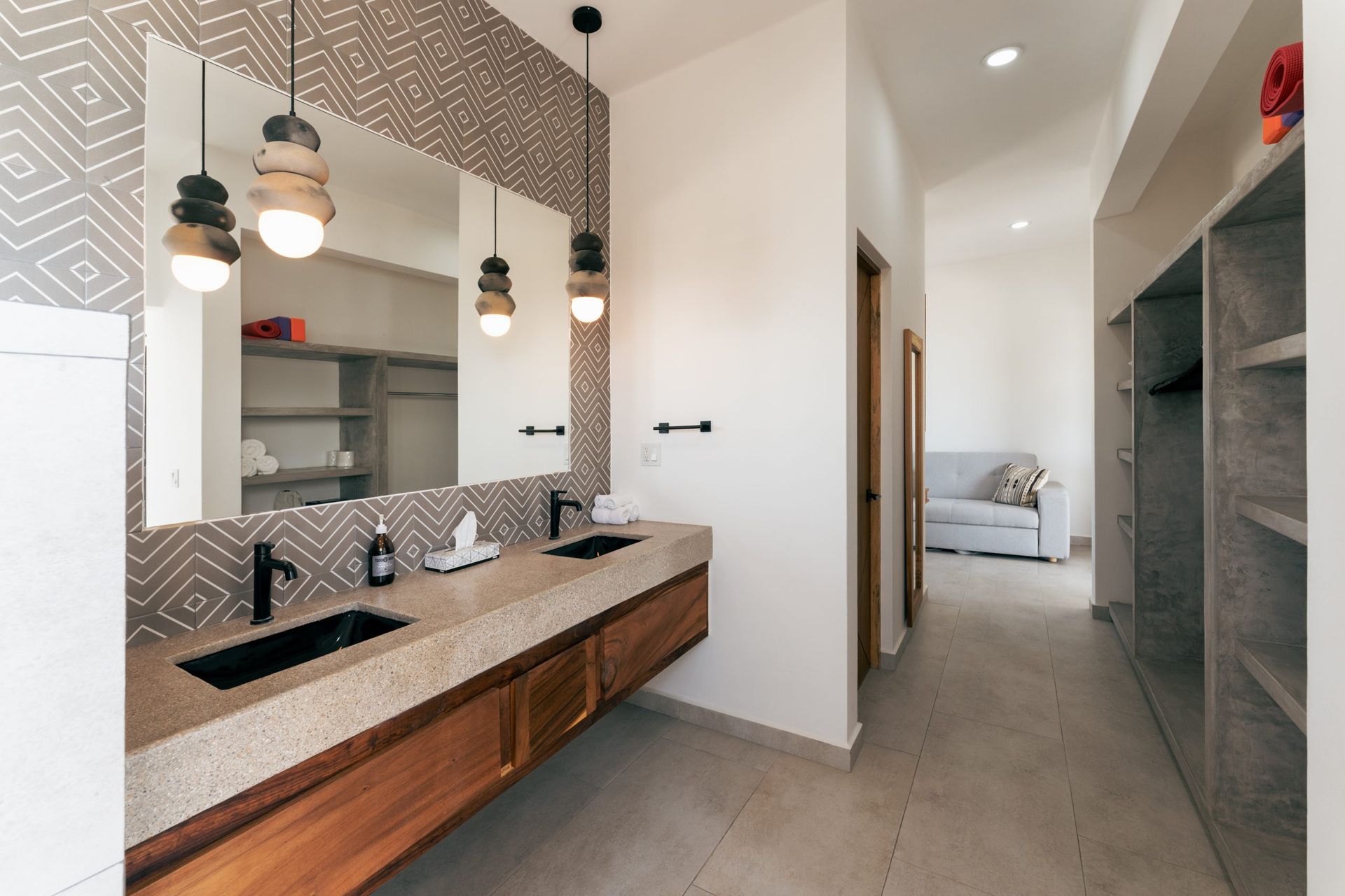 Bathroom with double sinks, large mirror, patterned wall, wood accents, and walk-in closet.