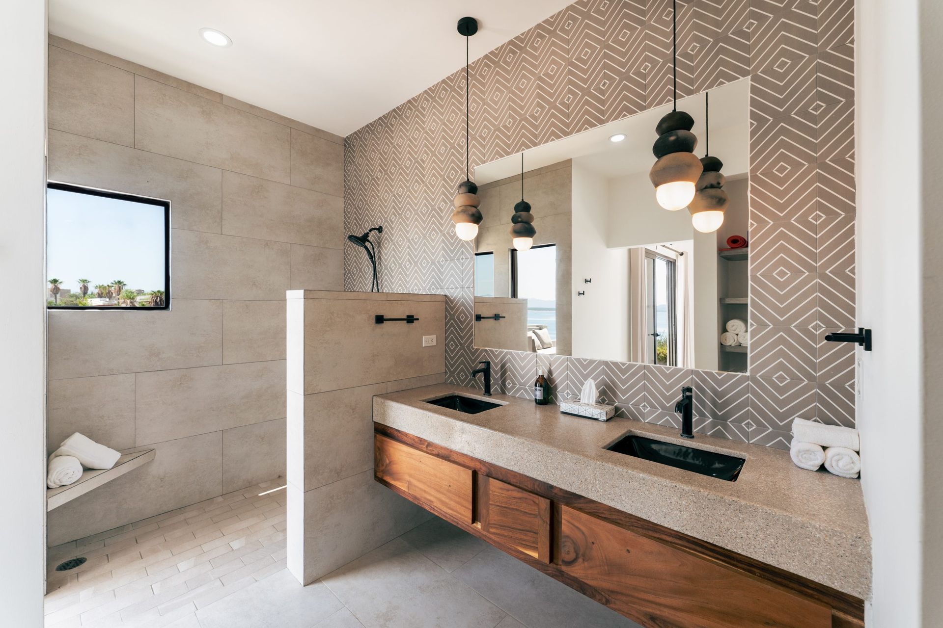 Modern bathroom with double sinks, large mirror, patterned tile wall, and shower.