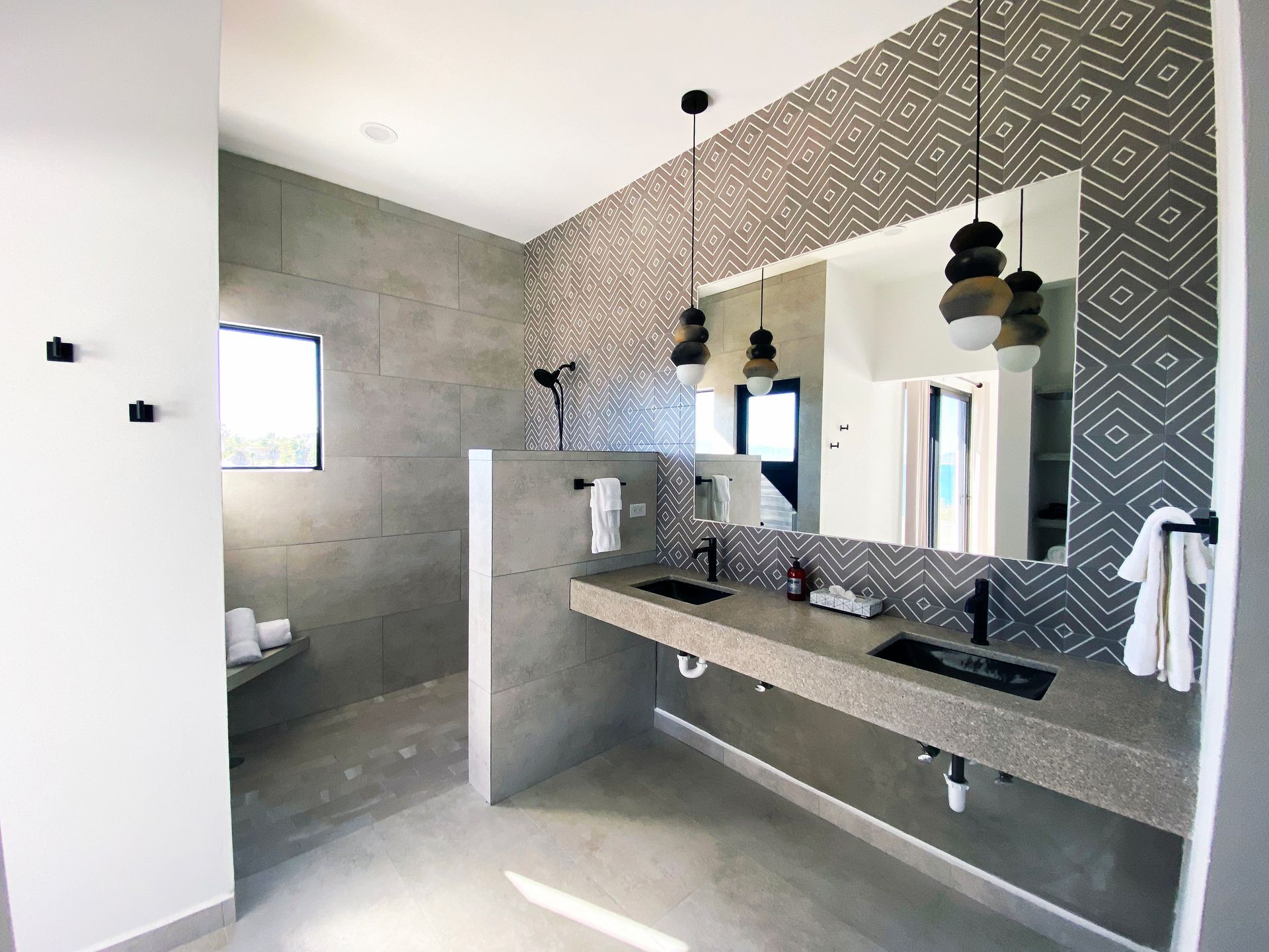 Modern bathroom with gray tile, double sinks, patterned backsplash, and hanging lights.