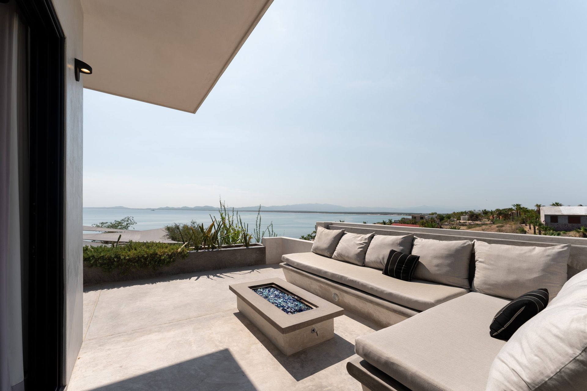 Rooftop lounge with beige sectional, built-in fire pit, overlooking a calm body of water.