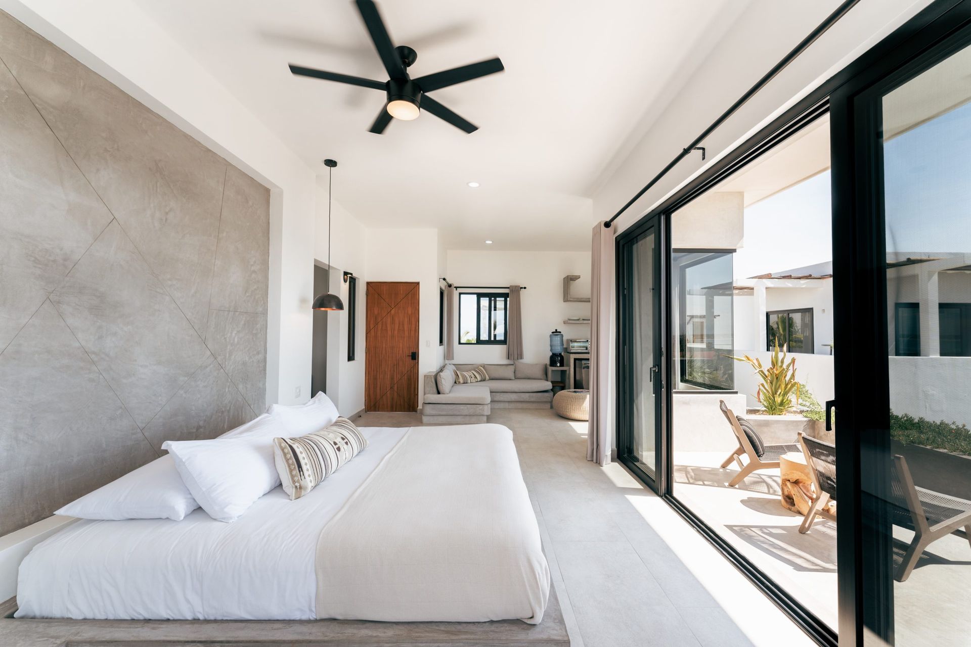 Bright bedroom with sliding glass doors to a patio. King bed, neutral colors, modern design.