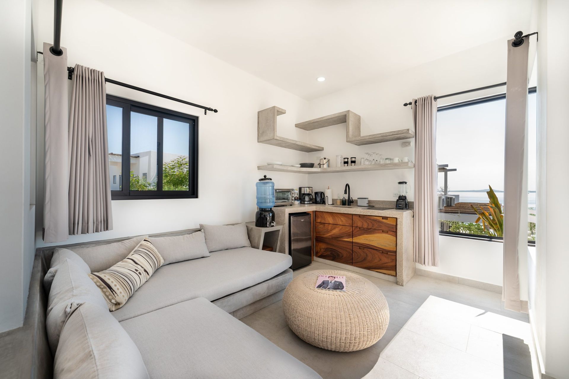 Modern living room with a gray sectional, kitchen, and ocean view.