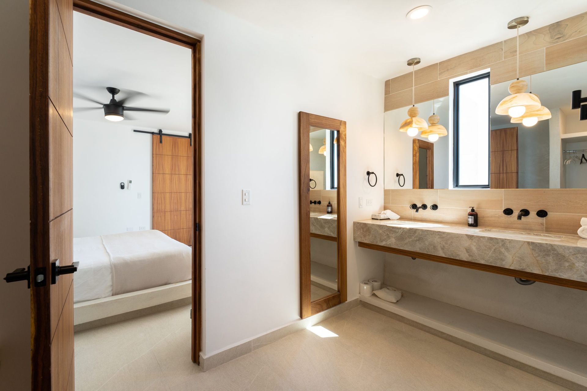 Bathroom with stone countertop, sinks, and a bedroom visible through a doorway.