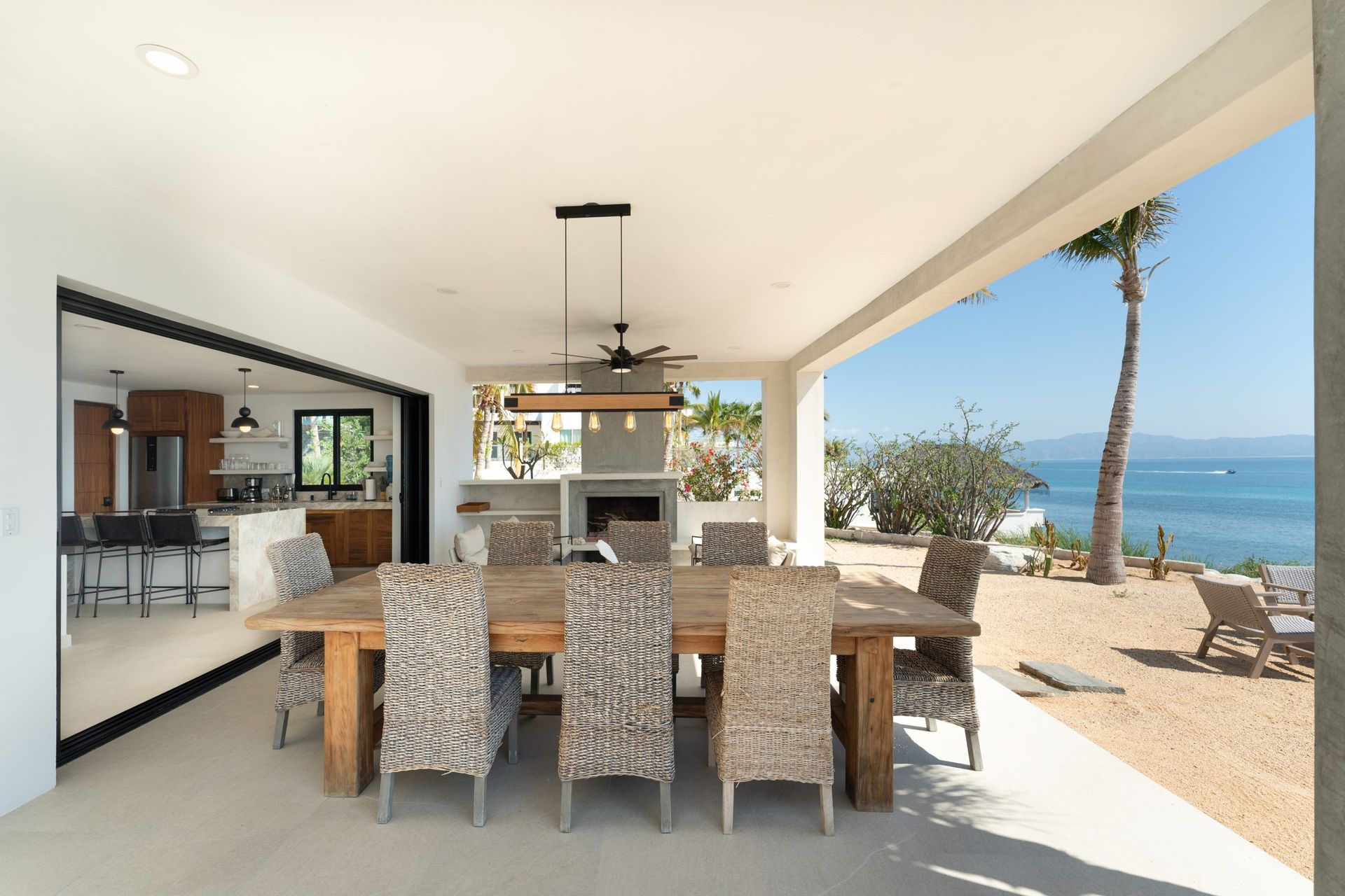 Outdoor dining area with a long wooden table, chairs, and ocean view.
