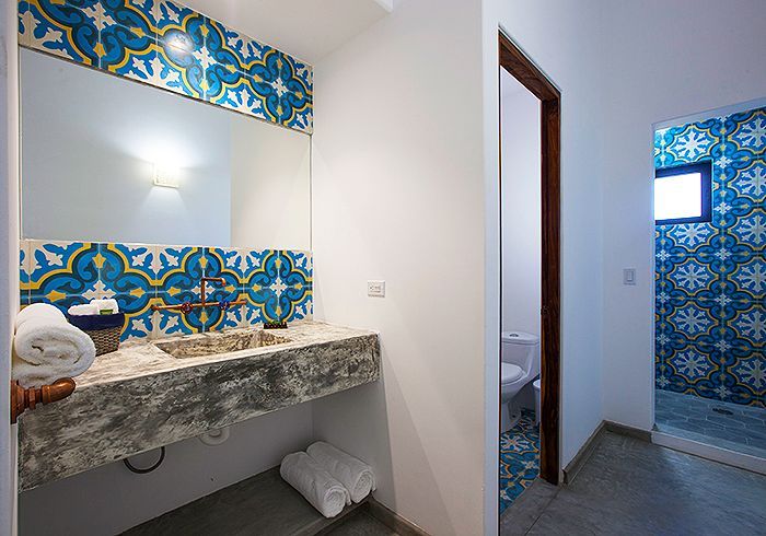 Bathroom with patterned blue and yellow tile, gray stone sink, white towels.